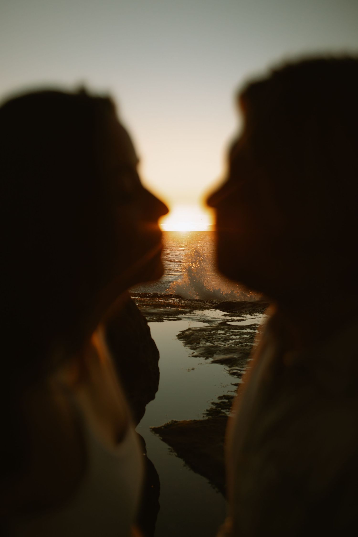 Silhouetted profiles frame sunset over coastal tidepools in romantic seaside moment.
