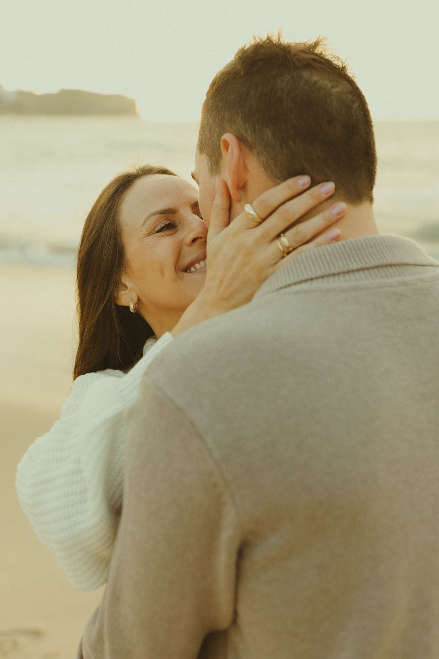 Intimate moment between couple on beach as woman lovingly holds partner's face during maternity shoot.