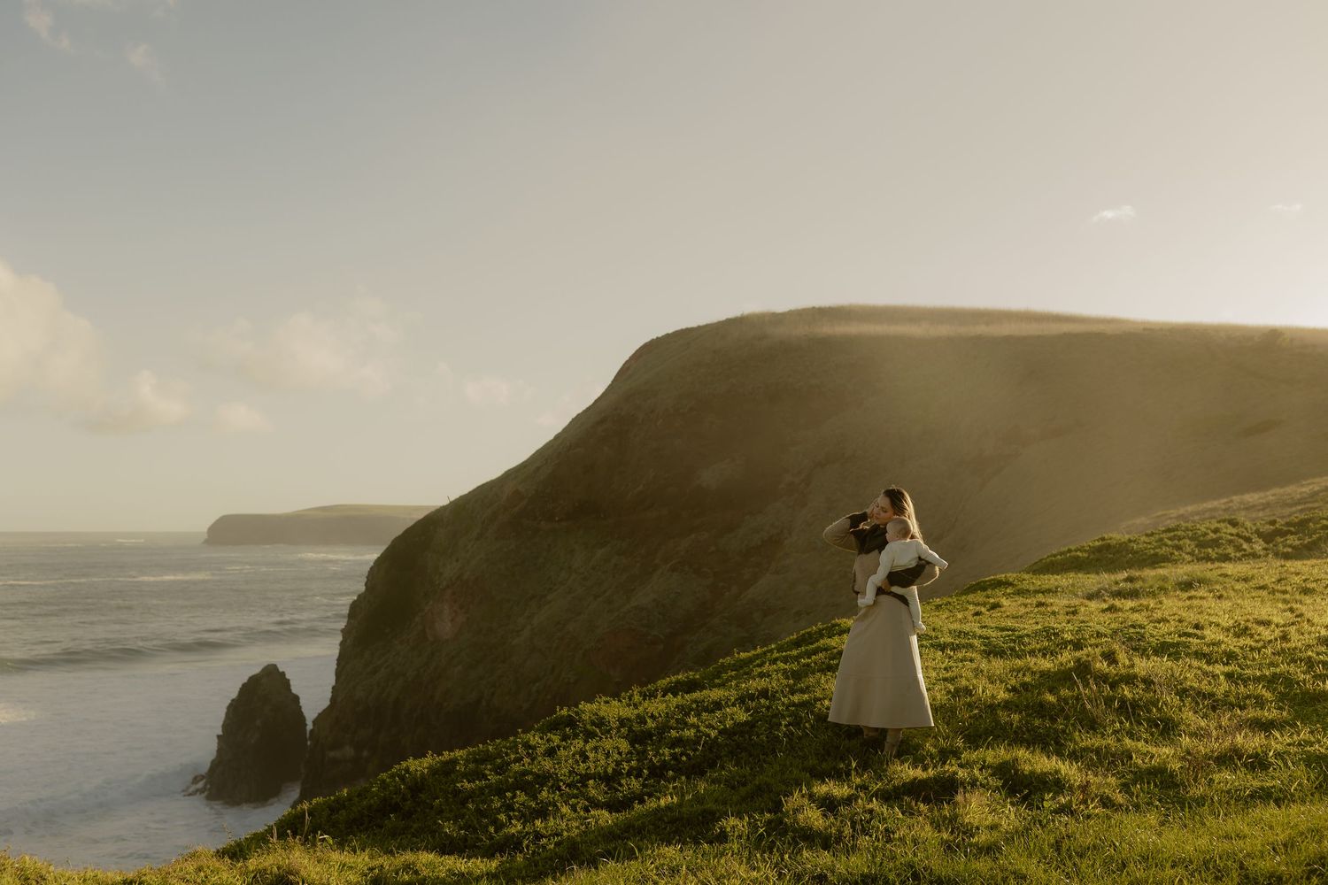 Couple embracing on lush green cliffs overlooking the ocean during golden hour at a coastal elopement.
