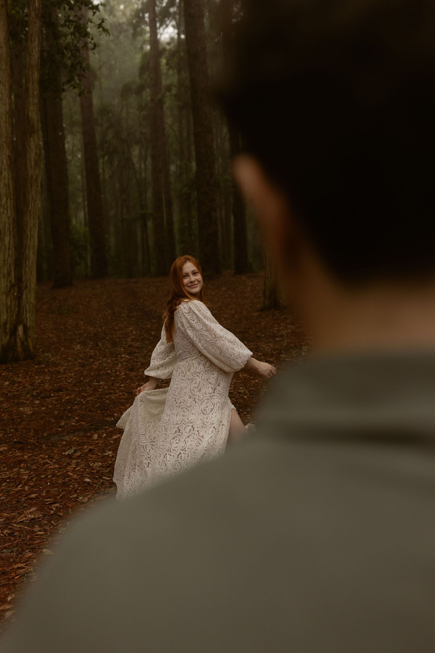 A couple in a forest setting creates dreamy wedding portraits with flowing white lace dress movements.