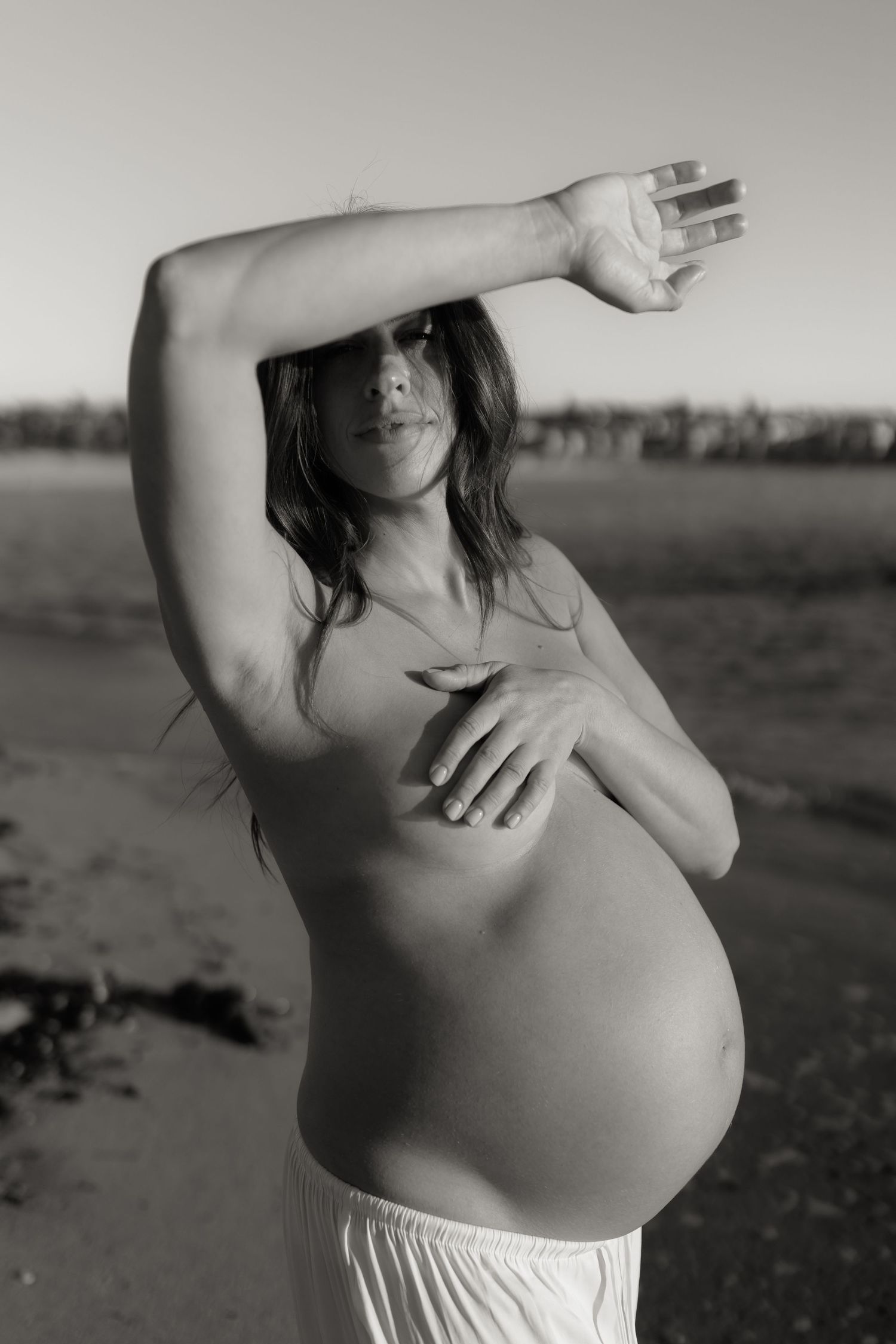 Black and white artistic maternity photos showing pregnant belly against natural backdrop.