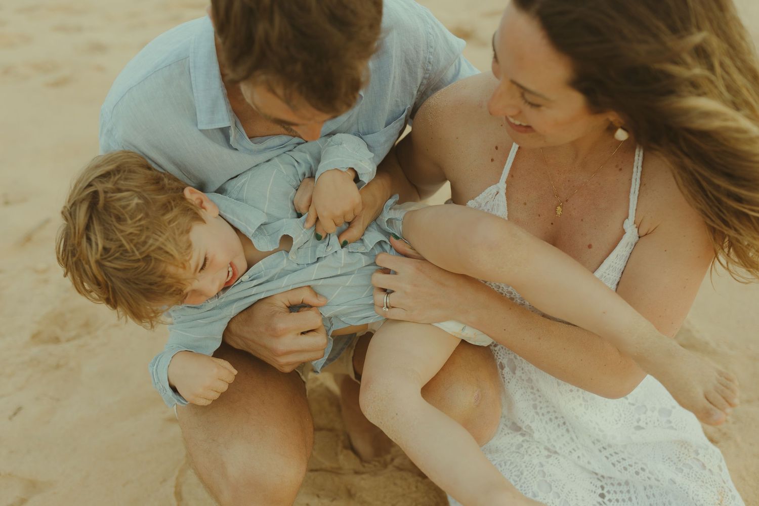 Romantic couple embracing while sitting on sandy beach at sunset.