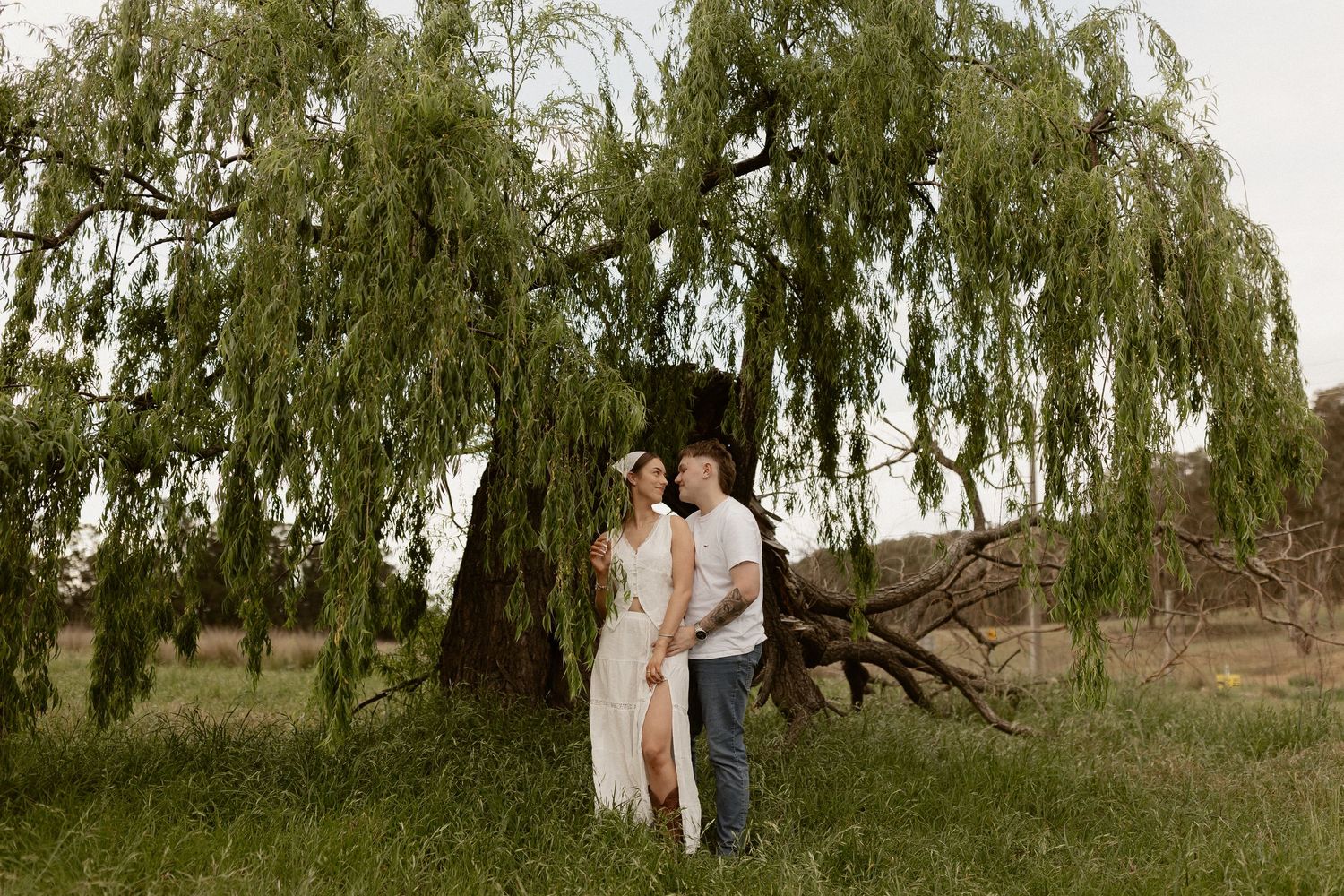 Two people walking together under weeping willow trees in a serene outdoor setting.