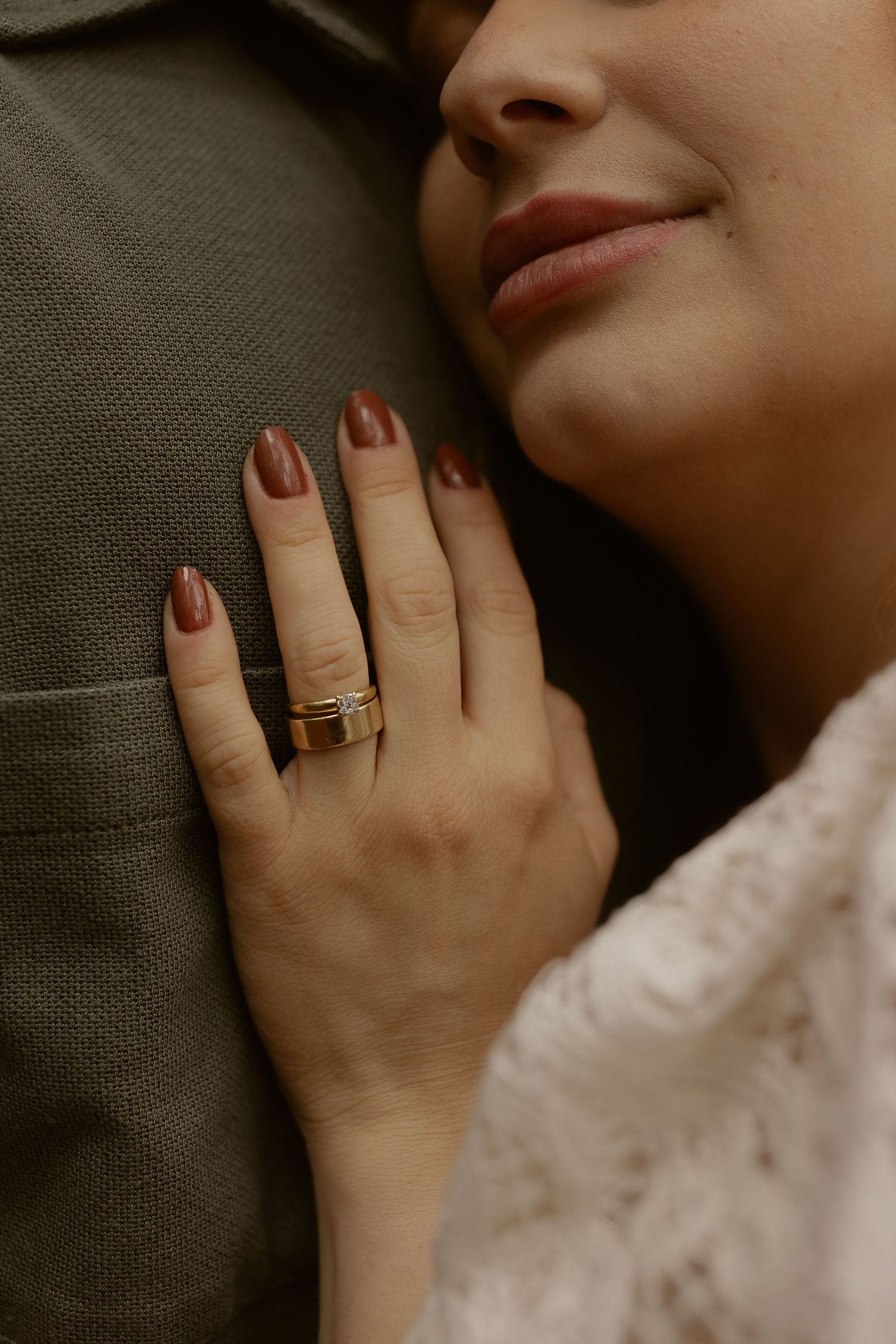 Close-up detail of a hand wearing an elegant ring against soft fabric with manicured nails.