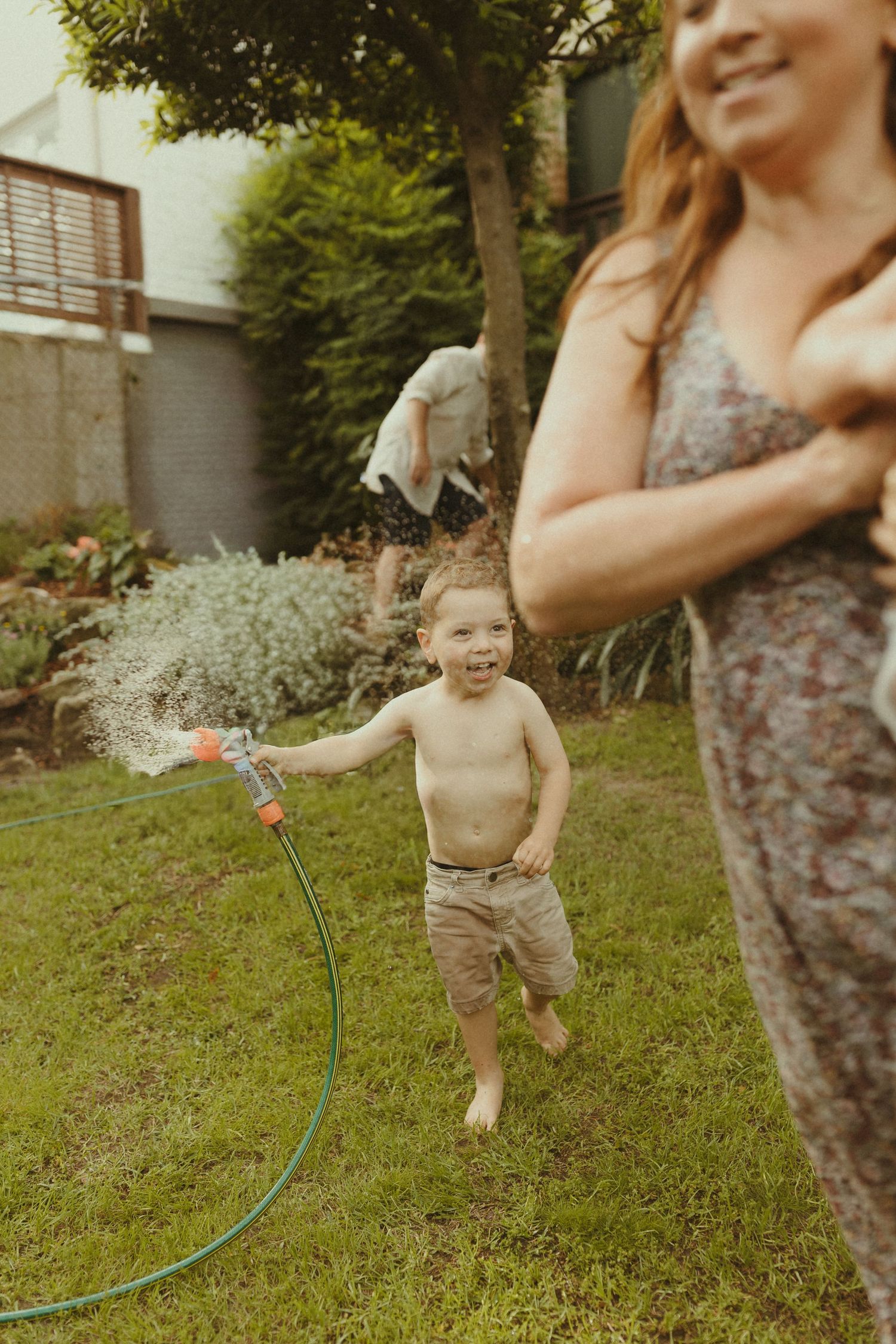 Child running through sprinkler in backyard on sunny summer day while playing in grass.