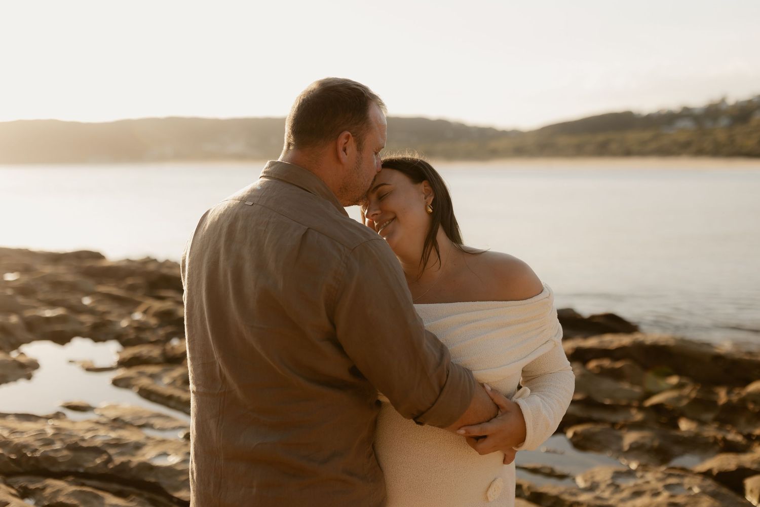 Couple embracing on rocky coastal overlook during sunset.