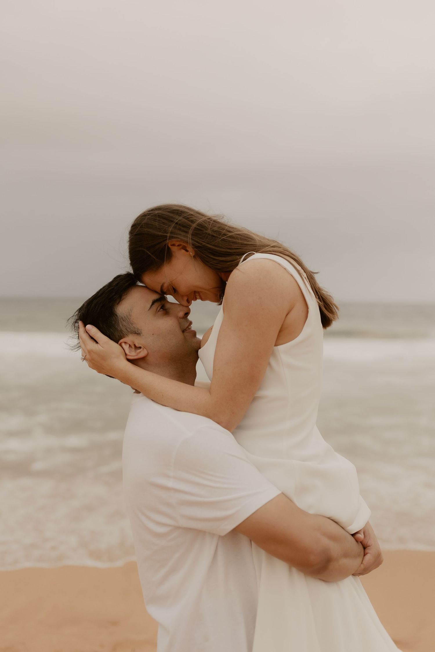 An intimate embrace captured on a sandy beach with overcast skies.