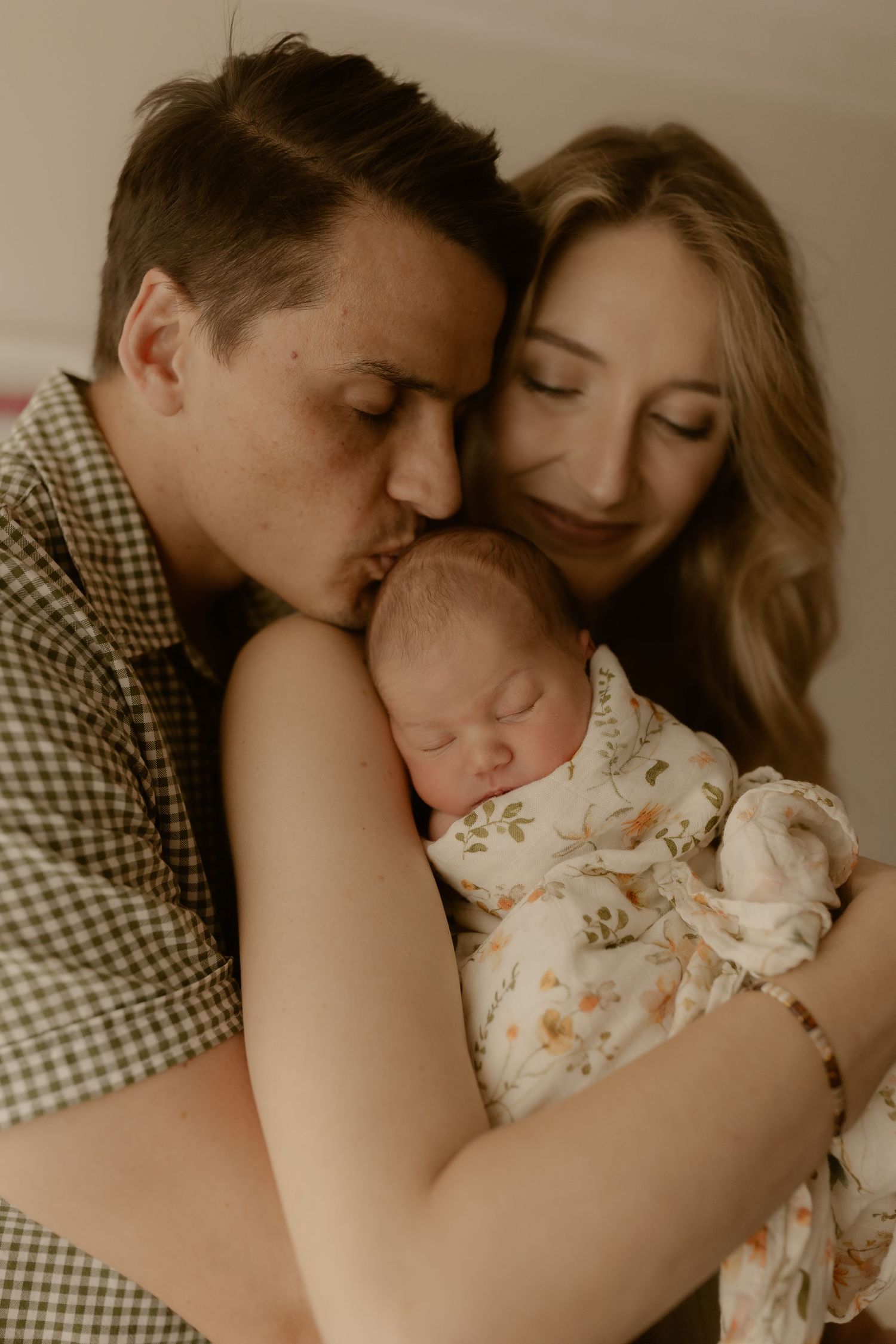 Intimate family moment with newborn baby in floral outfit resting between parents.