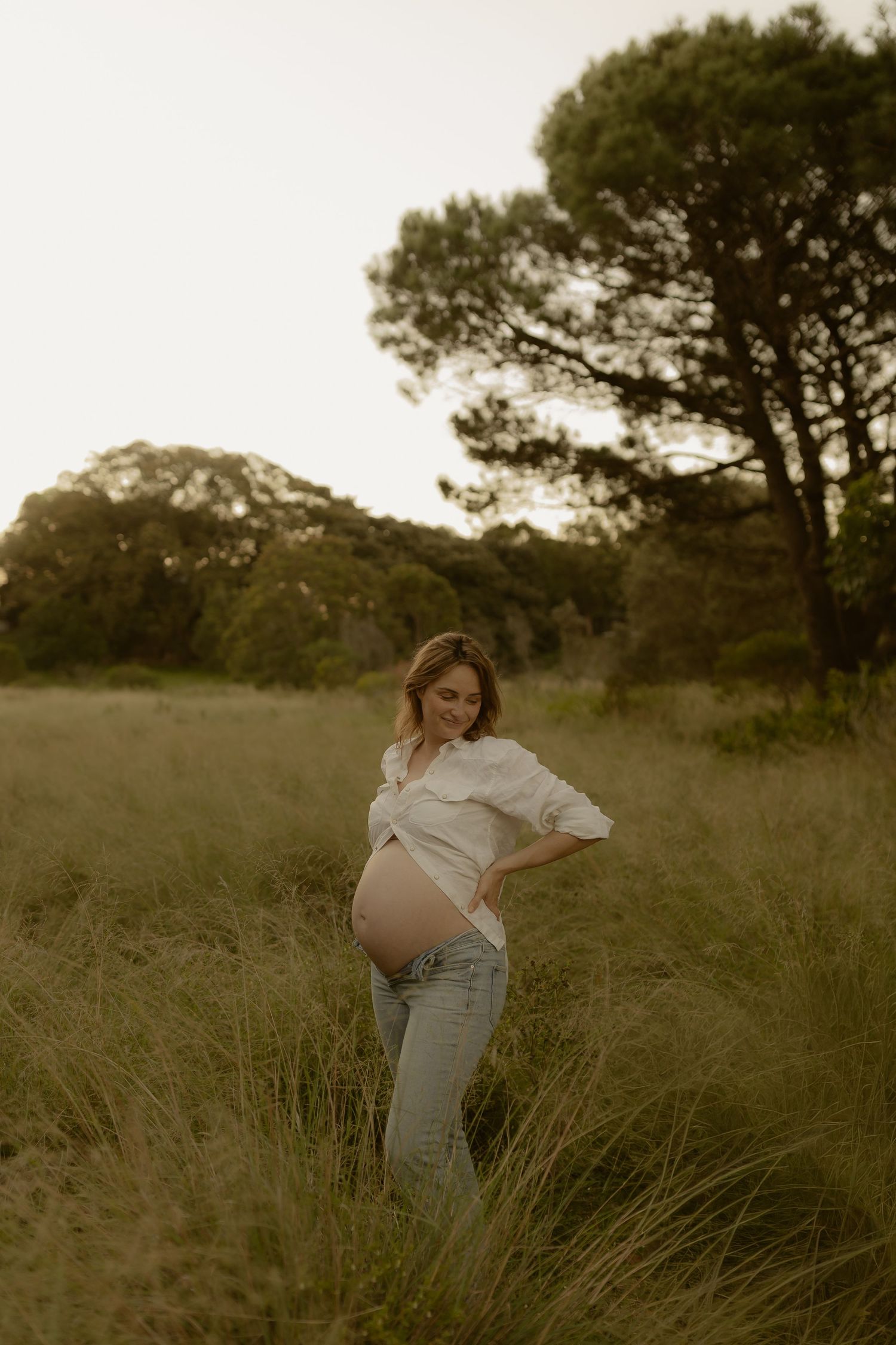 A joyful maternity photoshoot in a sunlit field with flowing white dresses and natural poses.
