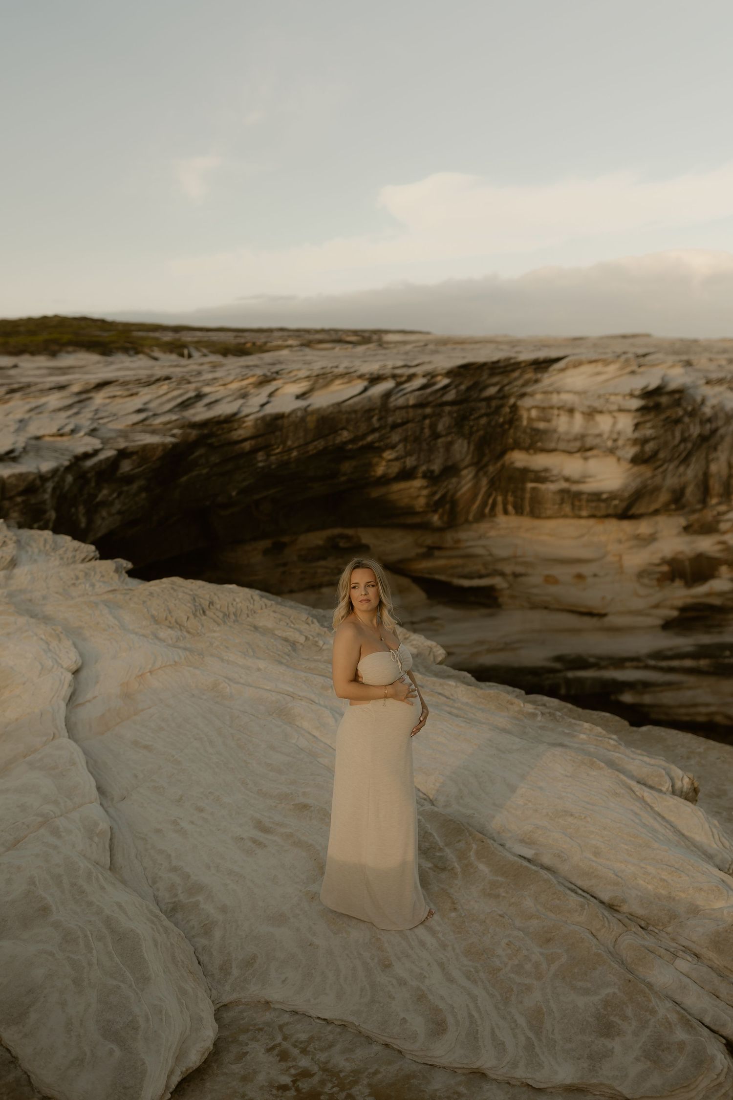 A figure in a light dress poses gracefully on smooth white rock formations at sunset.
