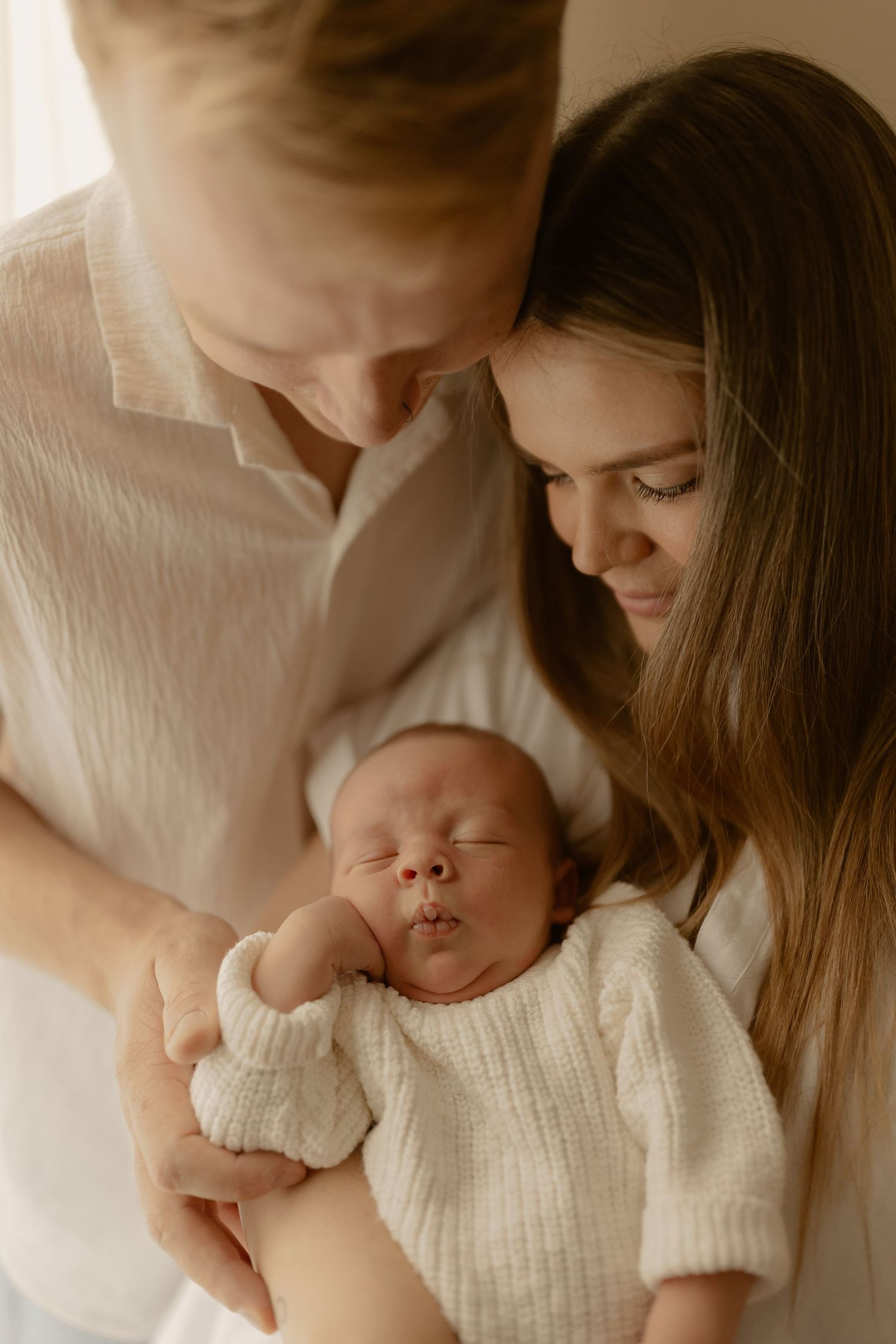 Tender family moment with newborn baby wearing white knitted sweater while being cradled.