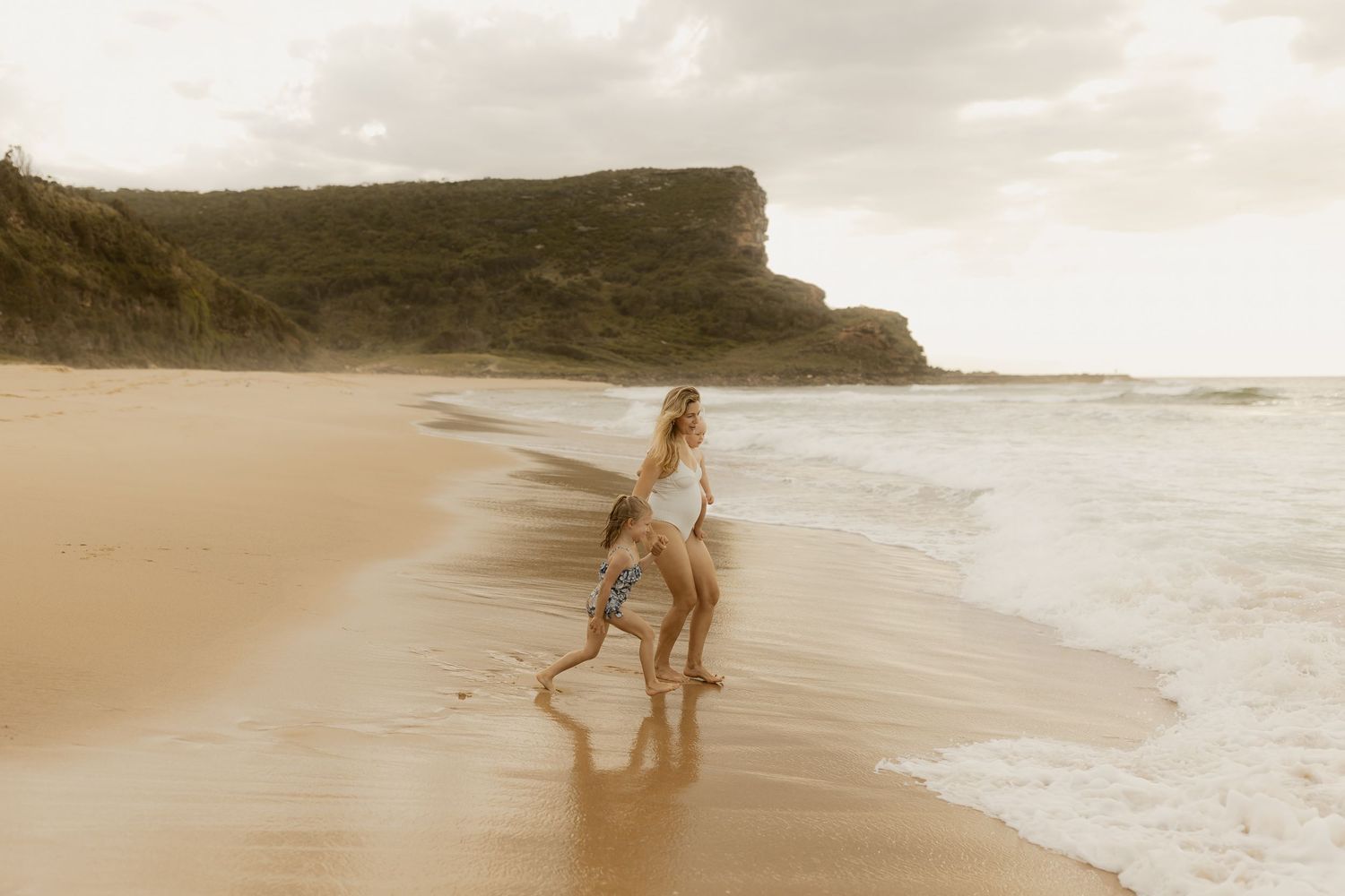 A dreamy sepia-toned beach scene shows figures walking along the shoreline beneath dramatic coastal cliffs.