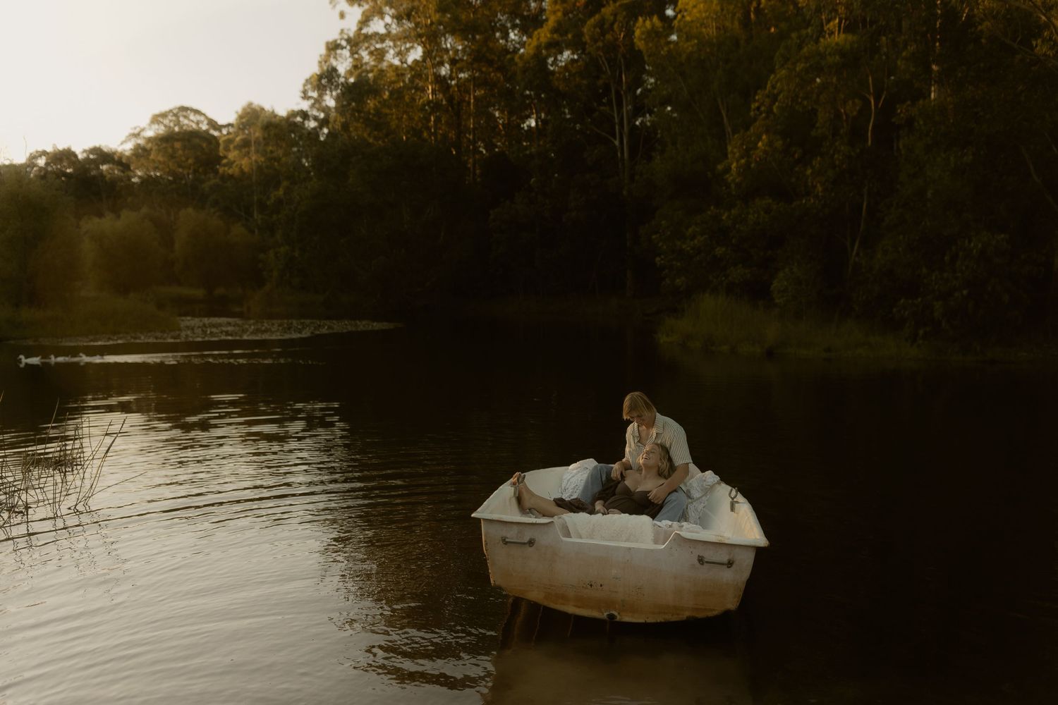 Small white boat drifting on tranquil lake waters at sunset.