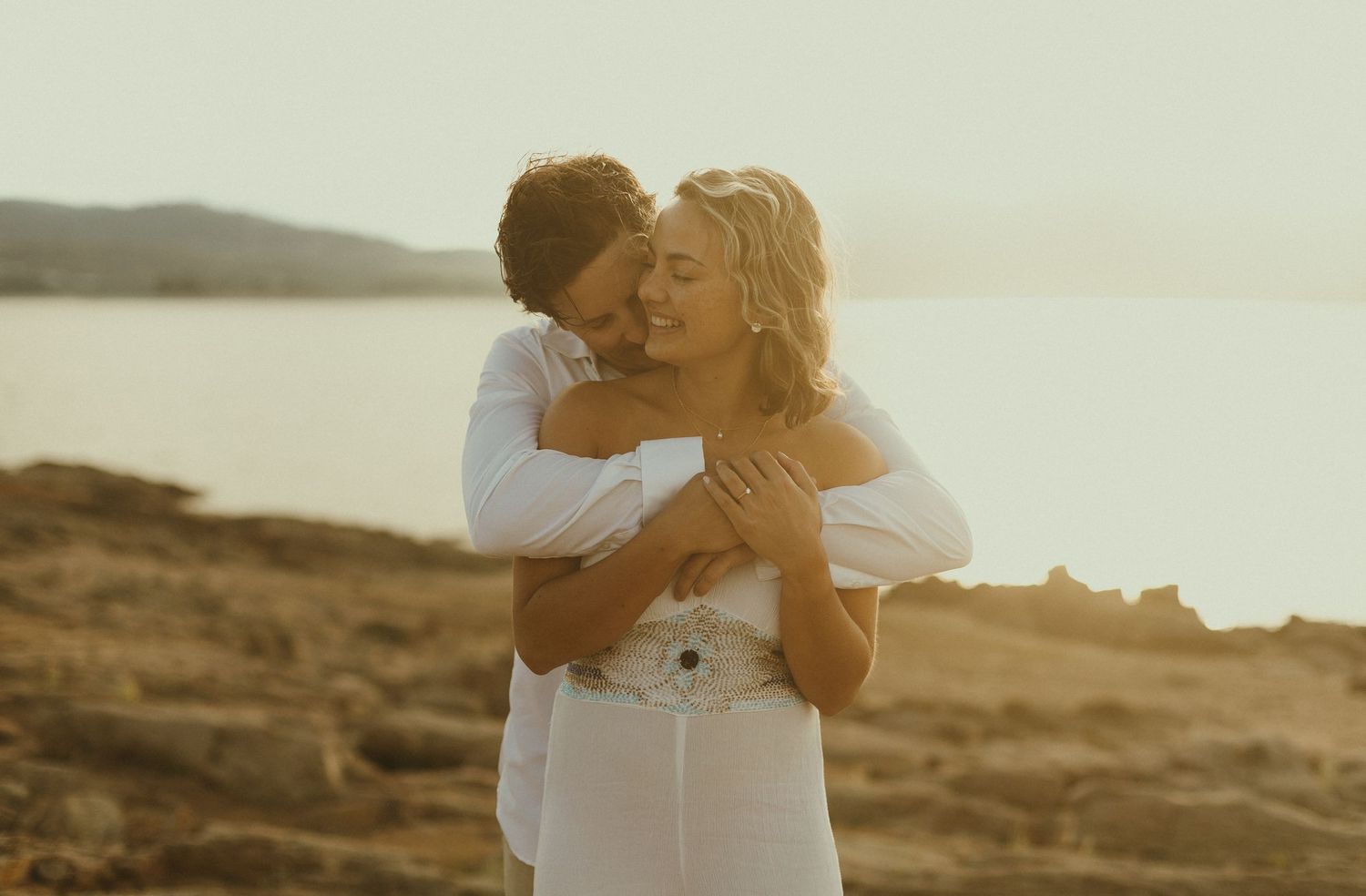 A tender moment between a couple at sunset on a rocky coastal landscape.