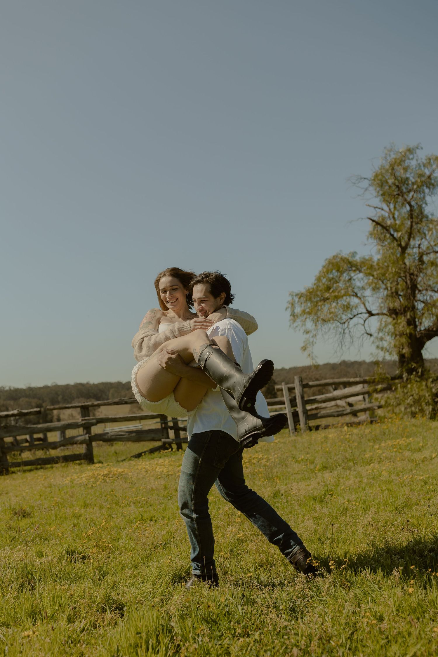 Playful dance sequence in a sunny field with wooden fence in the background.