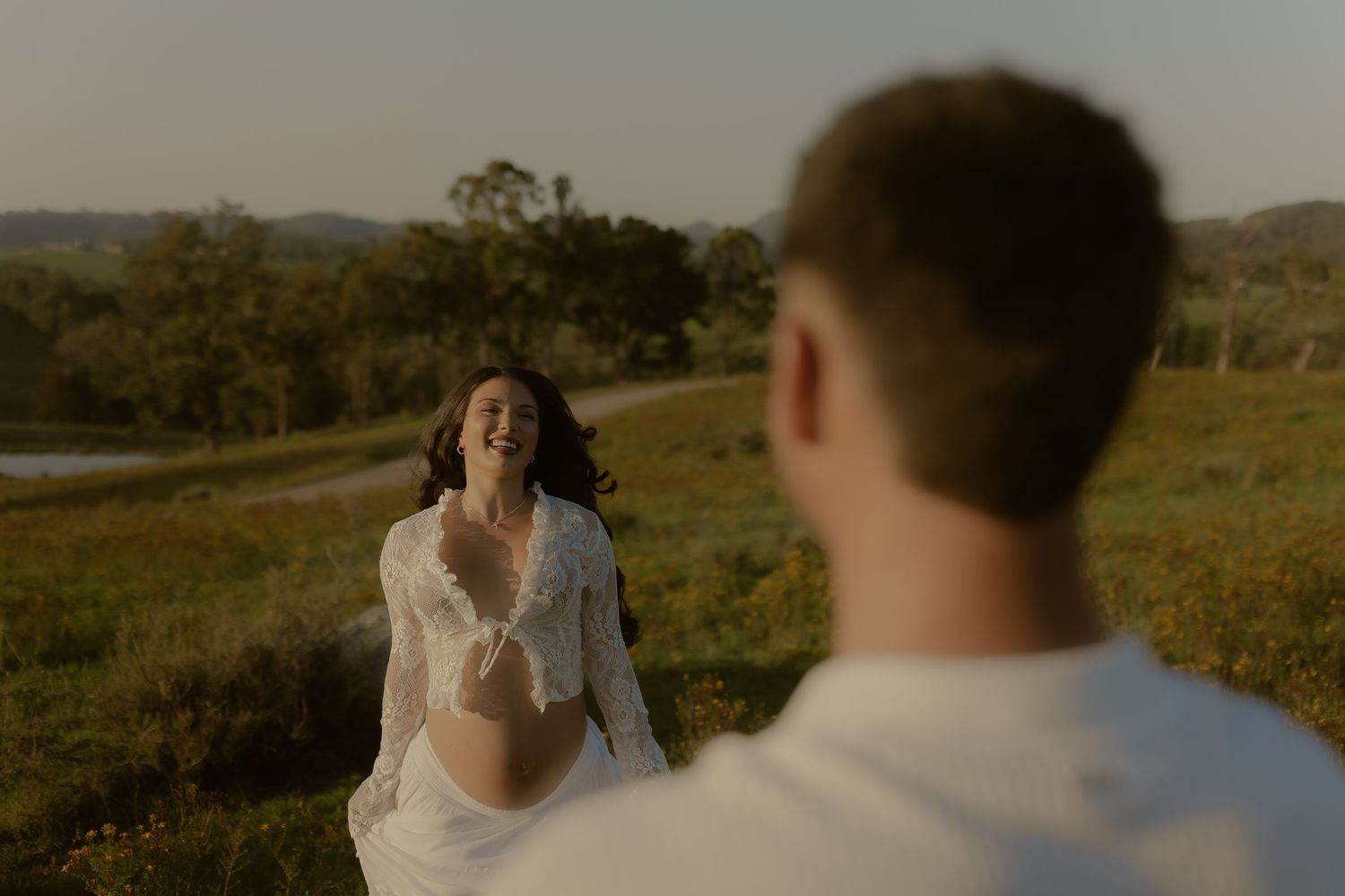 A romantic moment captured between two people in a sunlit field with mountains in the distance.