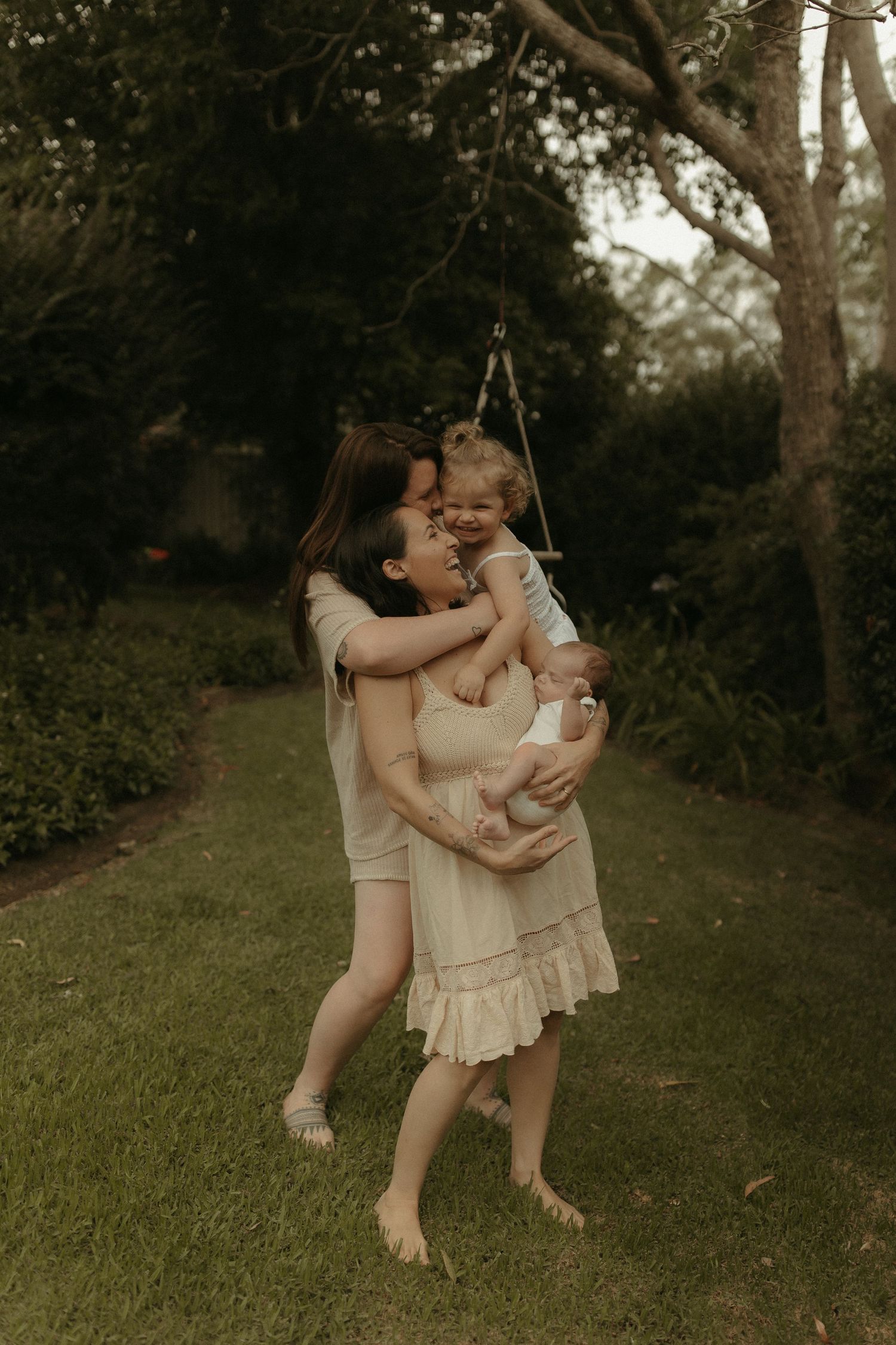Playful outdoor family photoshoot in a garden setting with coordinated cream-colored outfits.