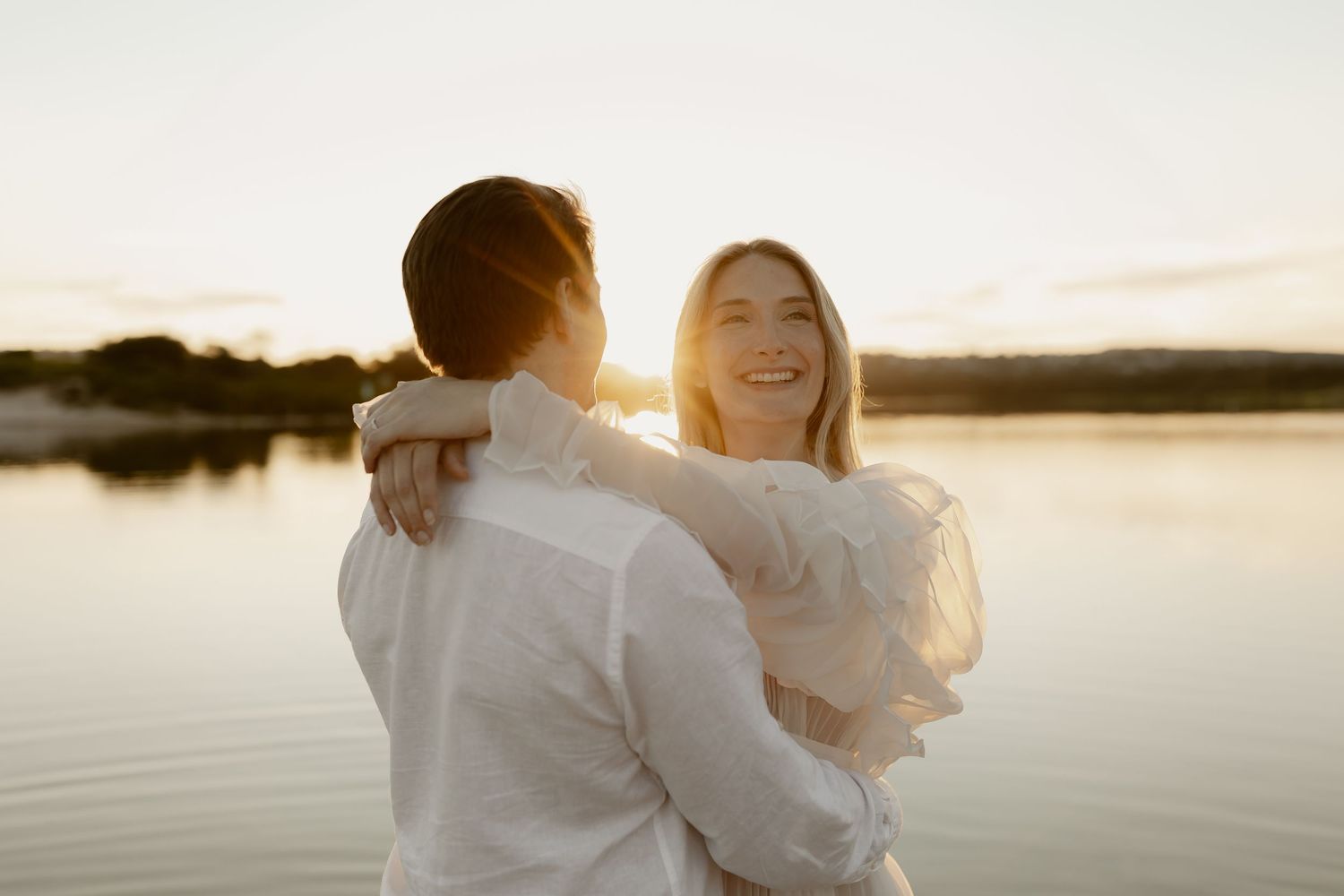 A romantic couple shares a joyful moment by the water during golden hour.