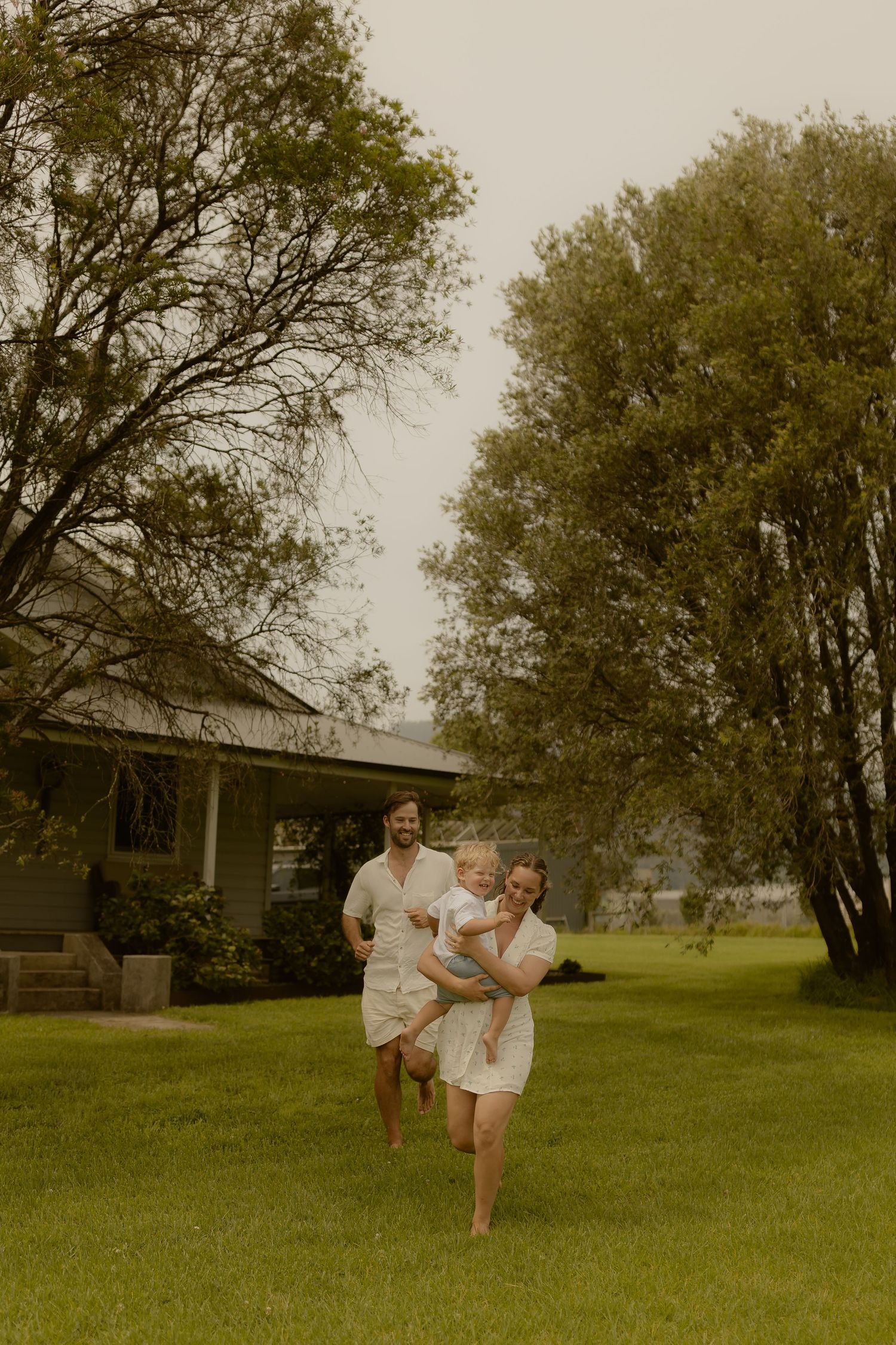People in white clothing playfully running and dancing in a grassy field on an overcast day.