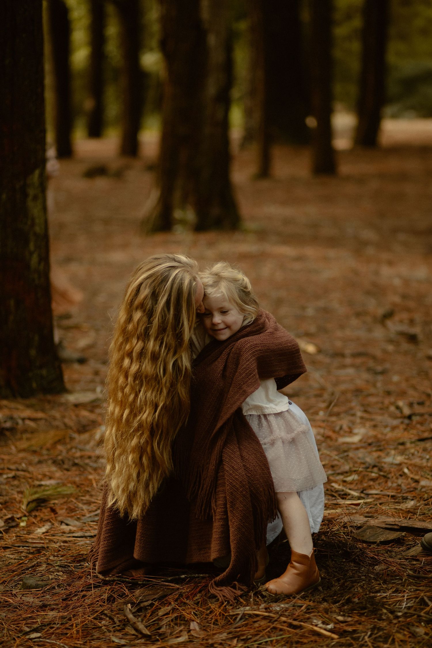 An intimate moment captured in a forest with warm brown tones and vintage-style clothing.