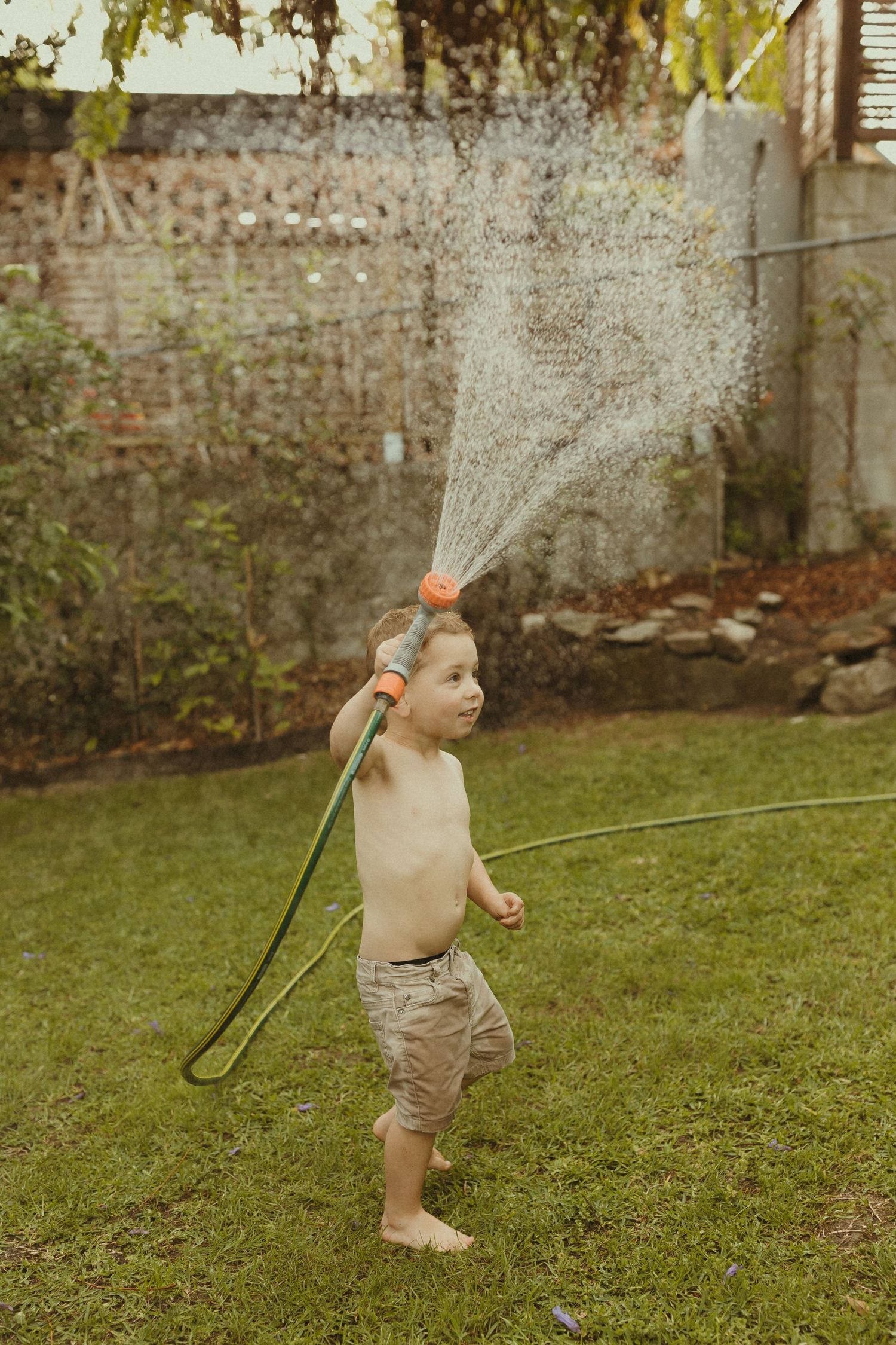 A sequence of photos showing a child running and playing with water from a garden hose in a grassy yard.