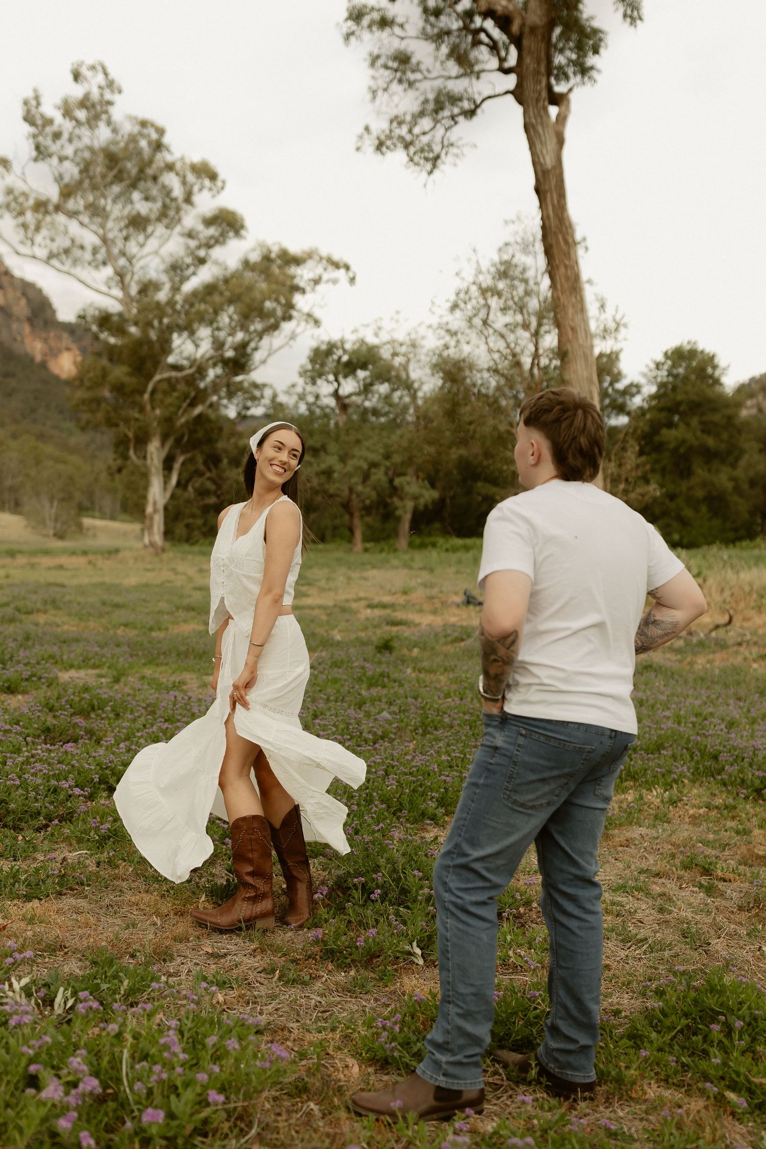 A romantic moment captured in an Australian bush setting with flowing white dress and casual country attire.