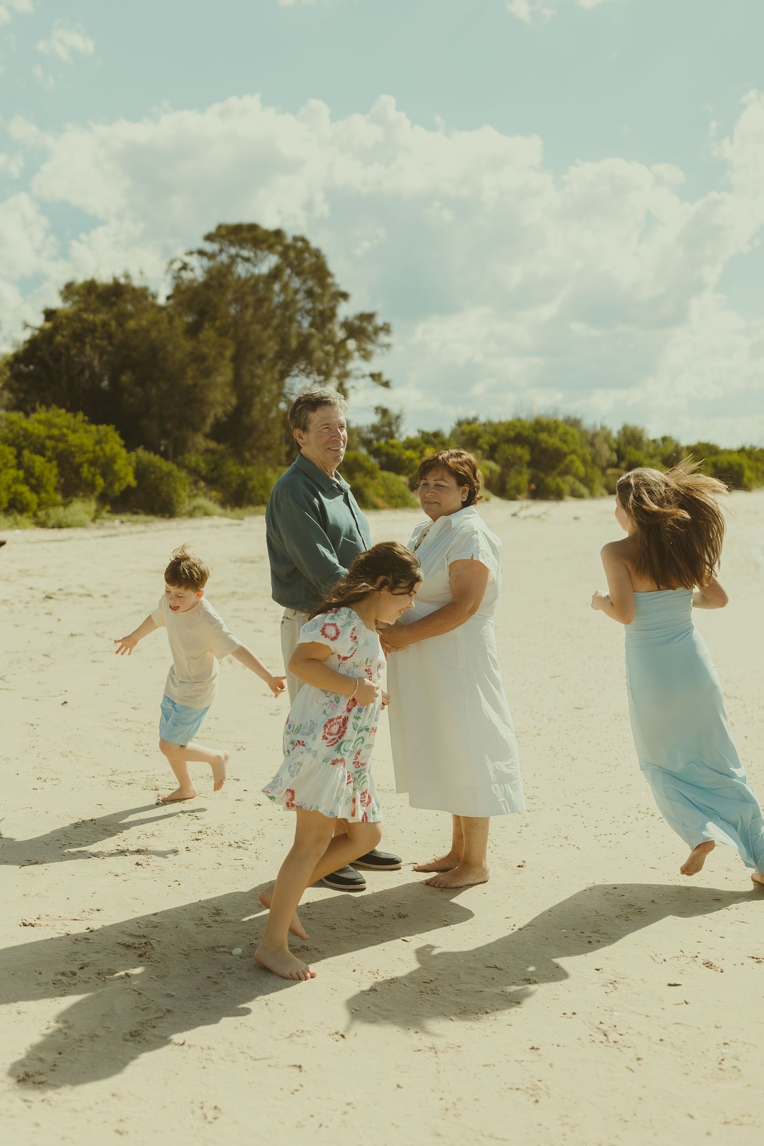 A playful sequence of a family running and playing together on a sunny white sand beach.