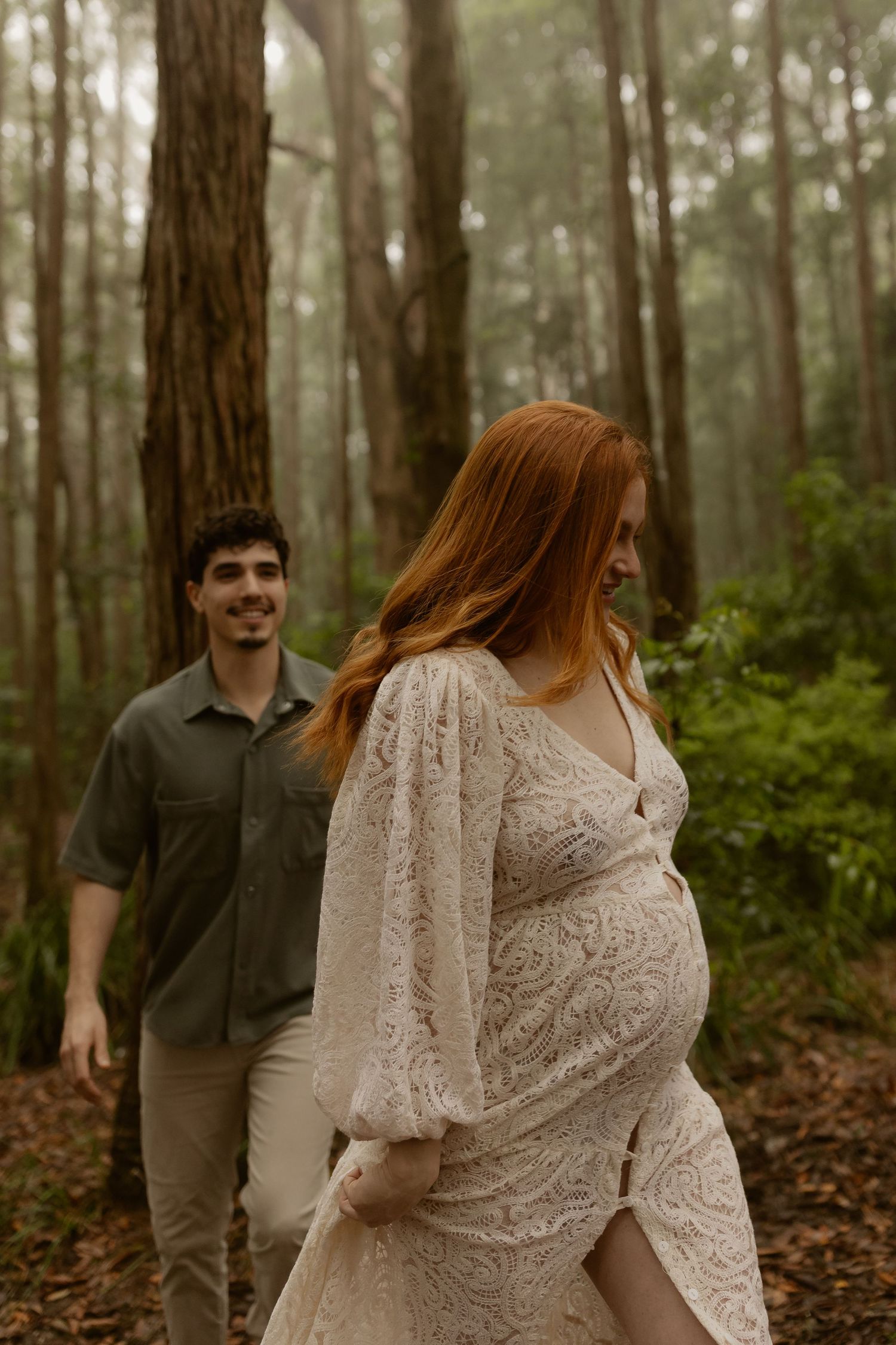 A couple in a wooded forest setting with the person in white wearing lace and spinning in a romantic moment.