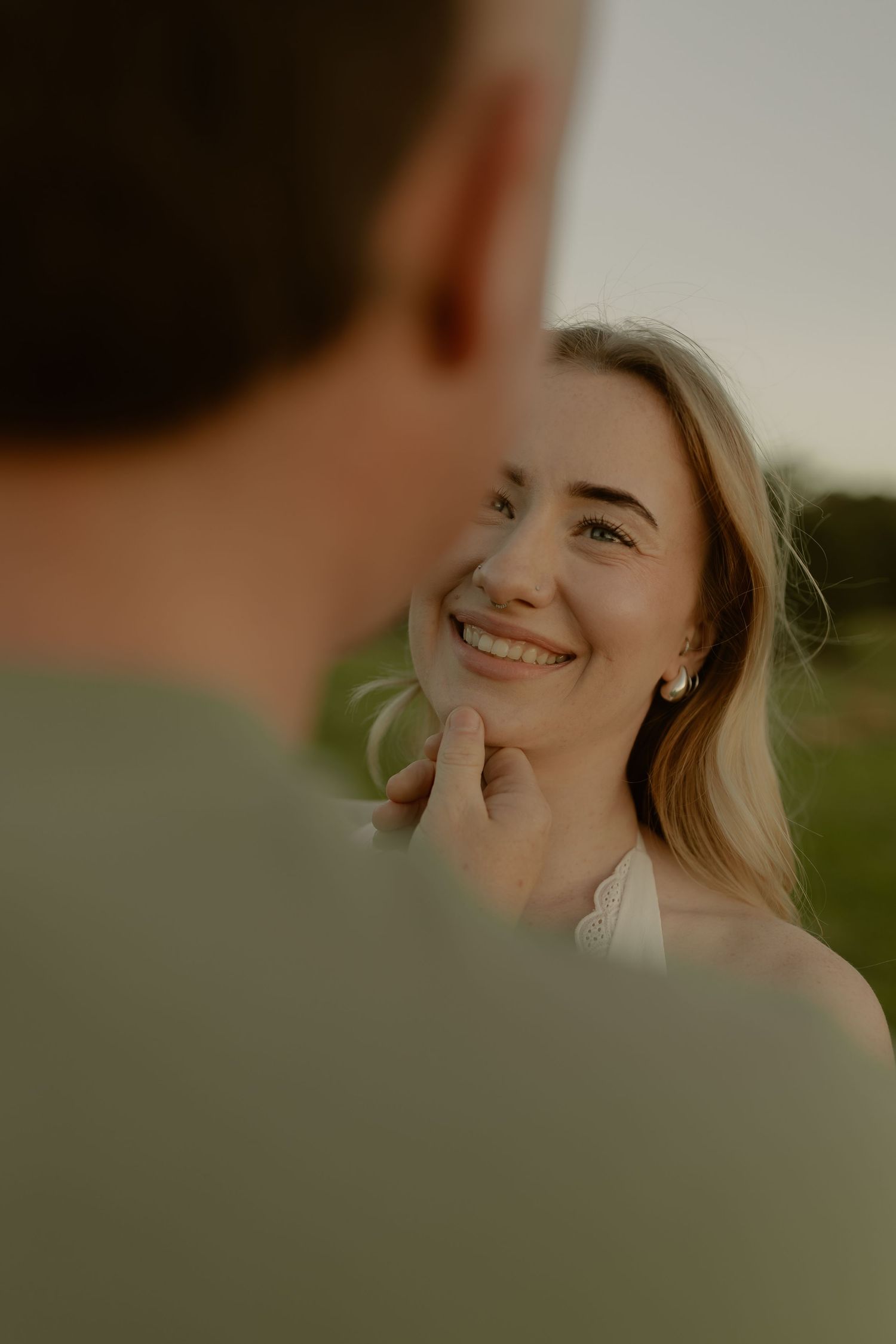 Smiling blonde woman gazes at man touching her chin in golden hour light.