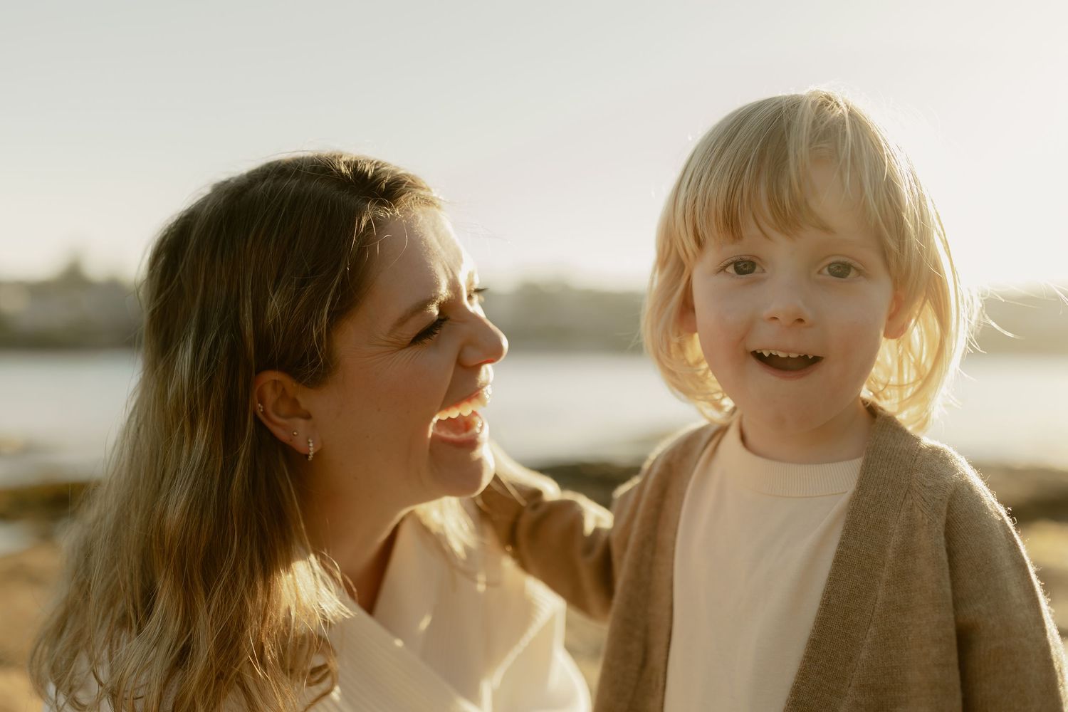 Smiling mother and her happy blonde toddler enjoying a sunny beach day together.