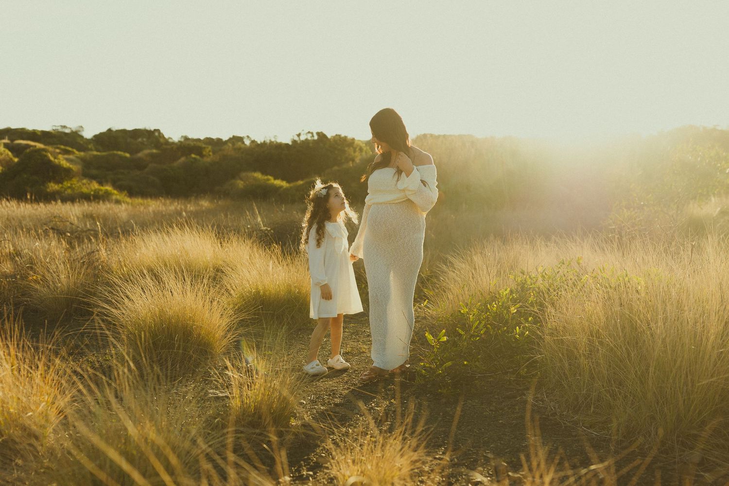 A dreamy sunset scene in a golden field with figures in white dresses illuminated by warm backlight.
