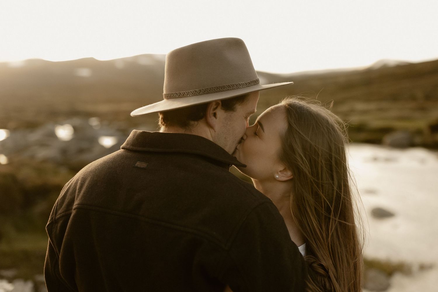 Silhouetted figures share an intimate moment against a warm sunset backdrop in a natural setting.