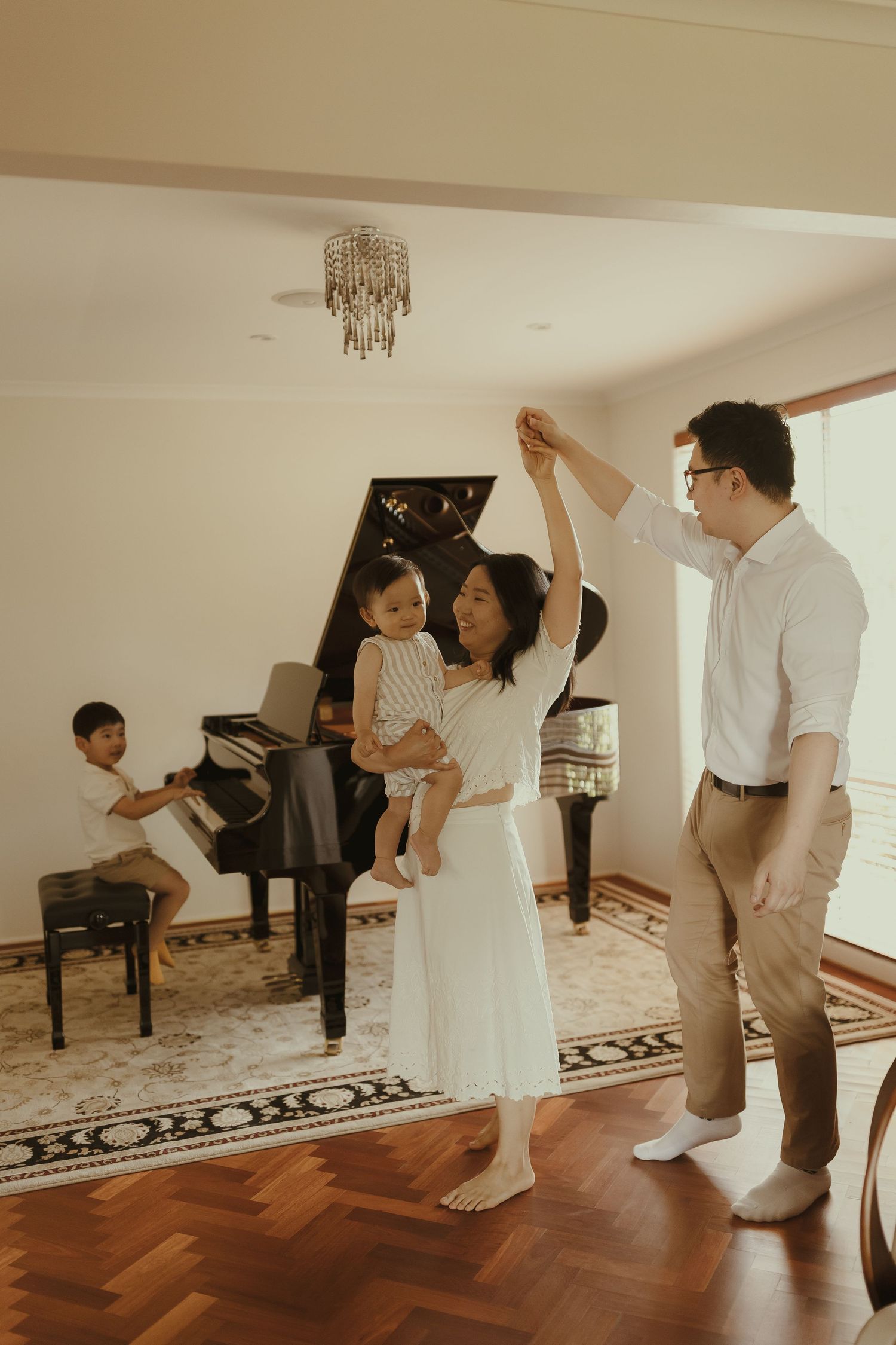A family enjoys dancing together in a living room with a grand piano and hardwood floors.