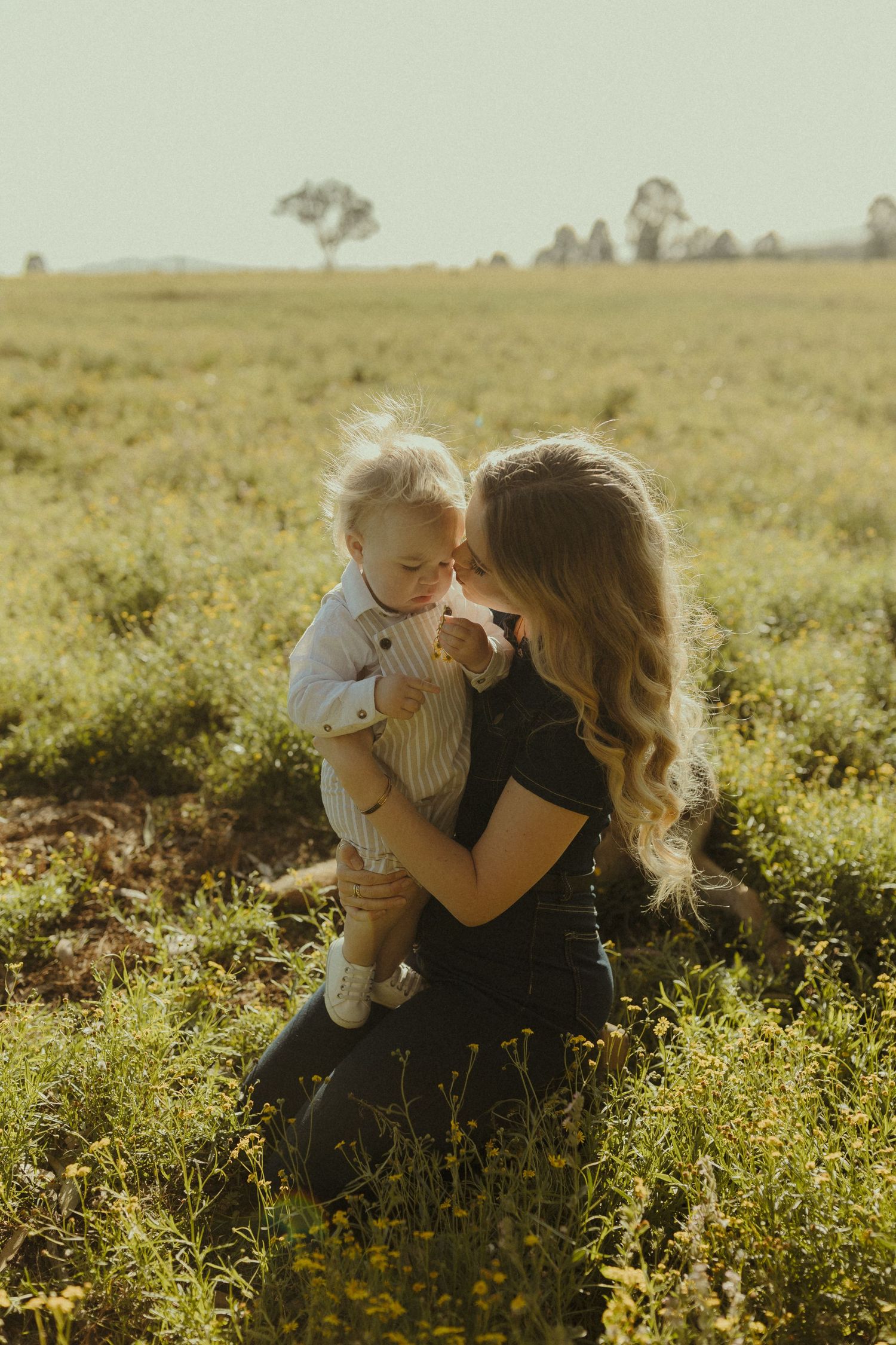 A tender moment between parent and child sitting together in a sunlit meadow with wildflowers.