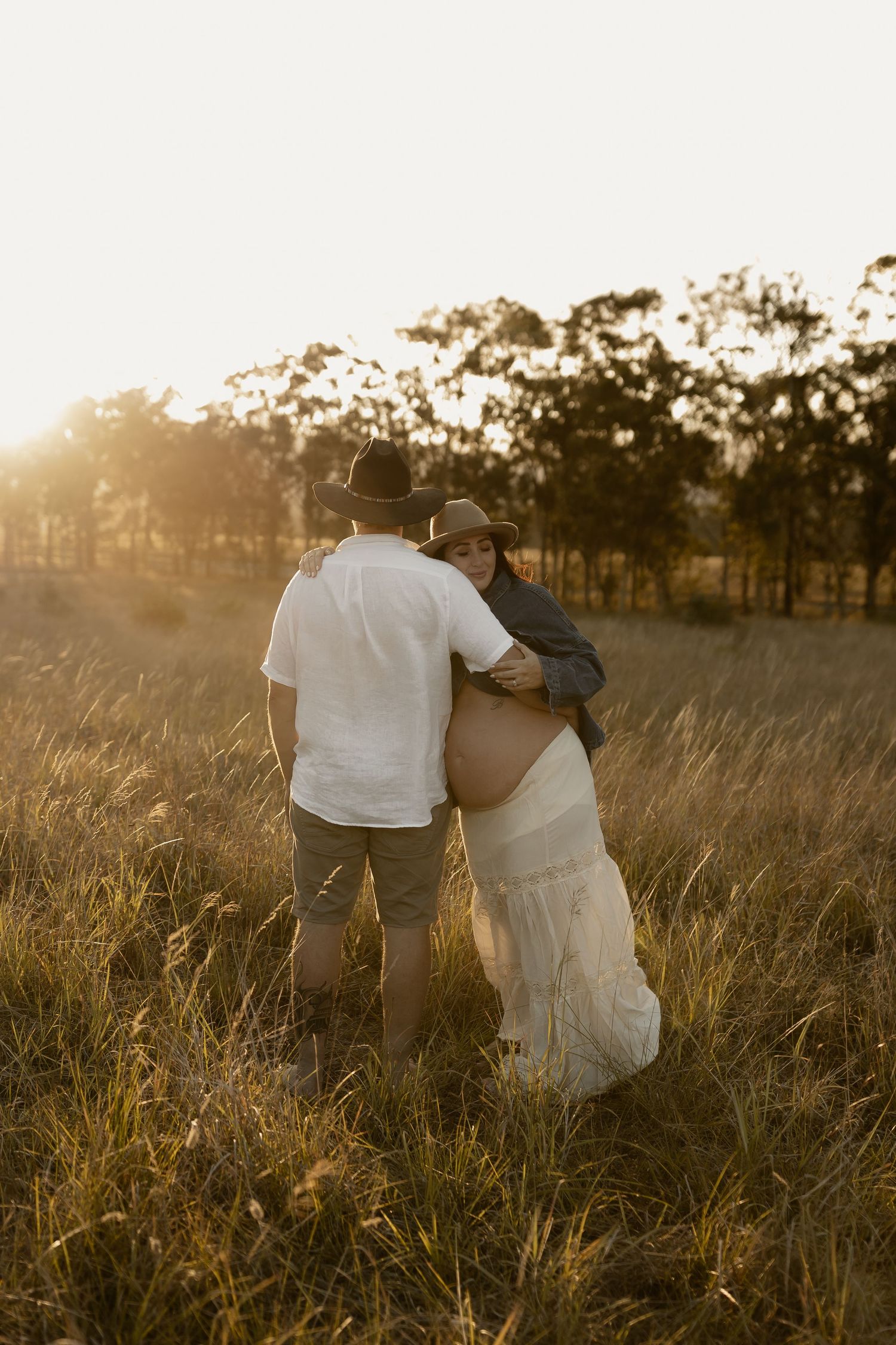 A couple embraces in a golden sunlit field at sunset, creating a romantic silhouette against the tall grass.