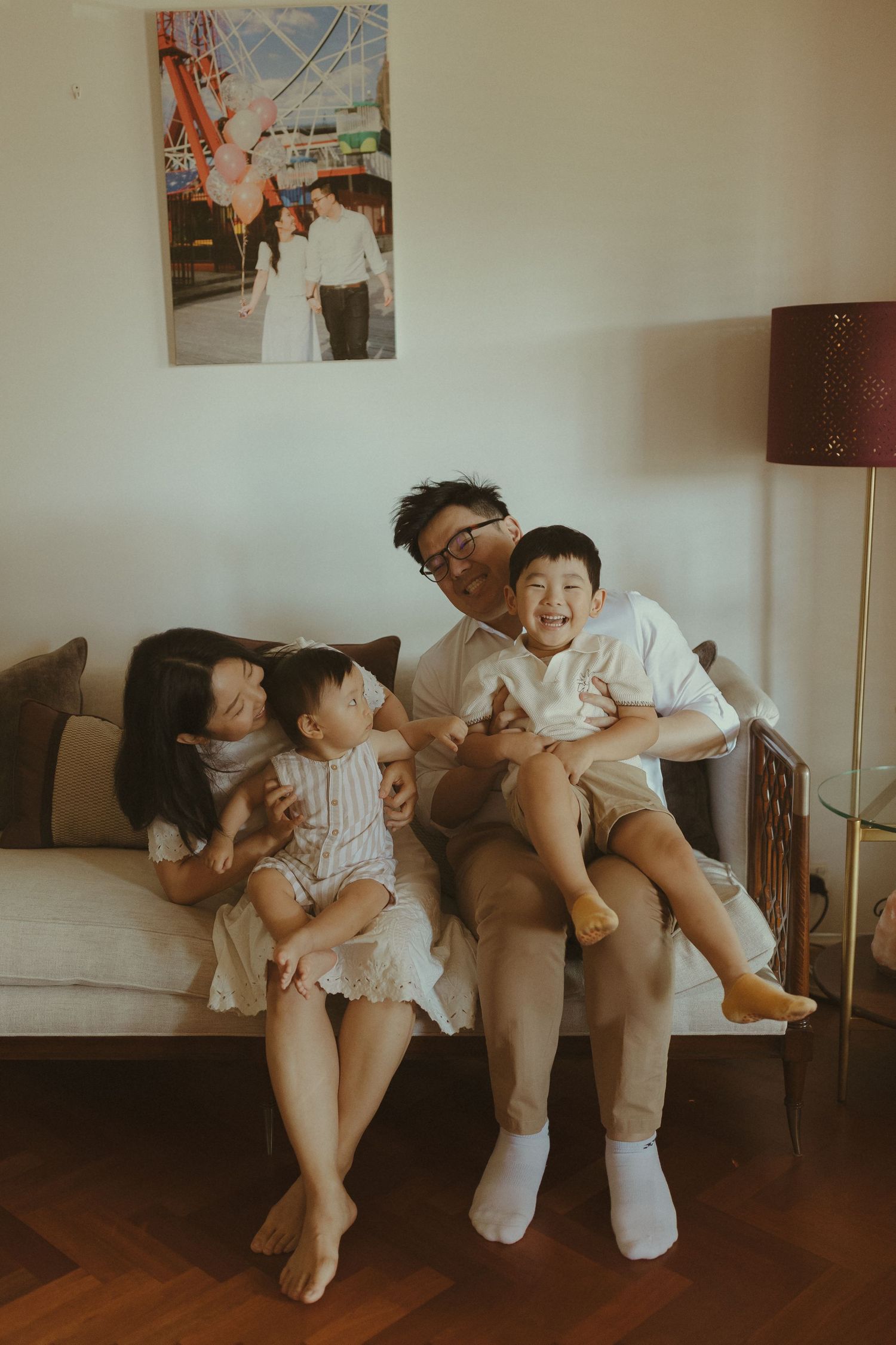 A family shares joyful moments together on a couch with a wedding photo visible on the wall.