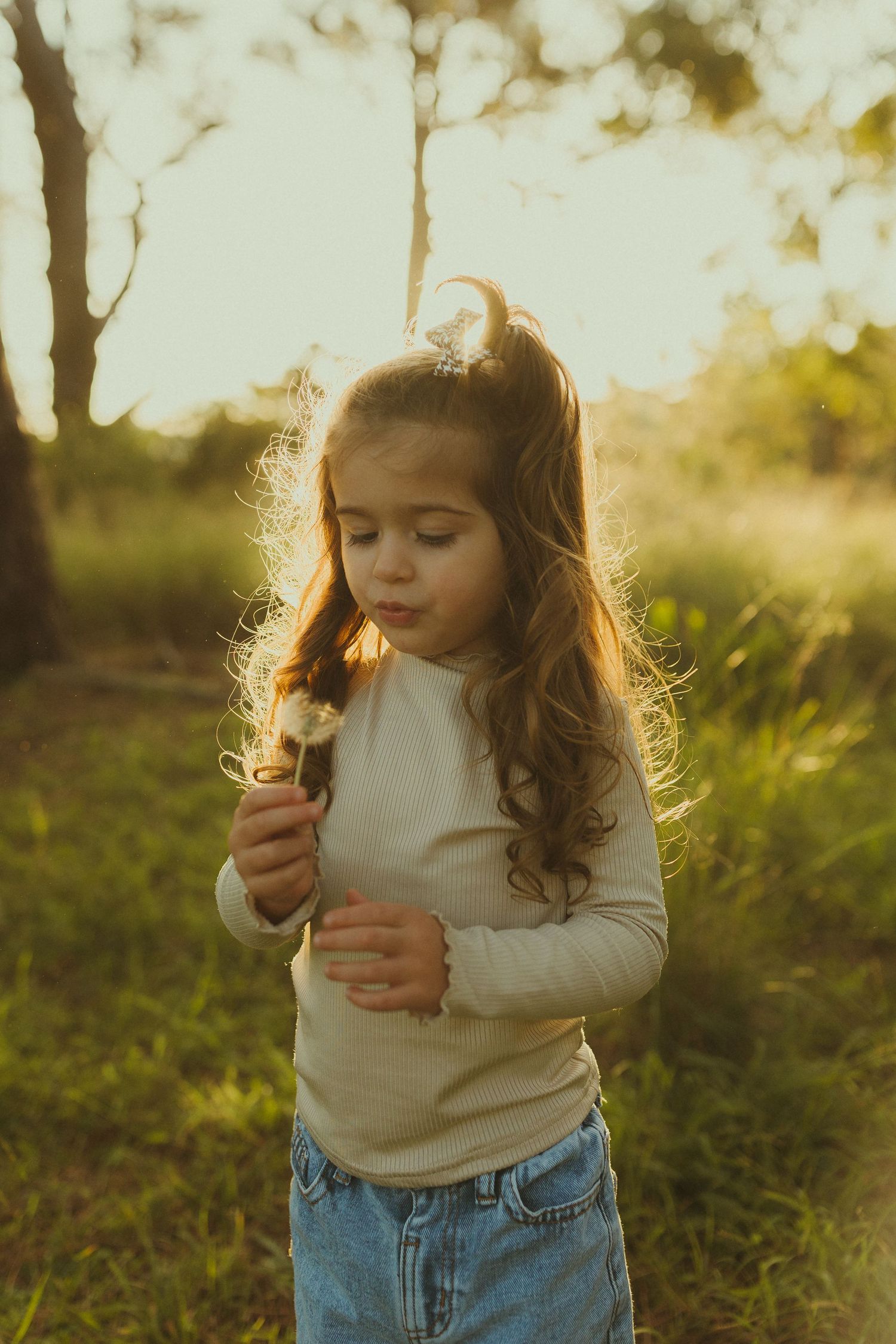 An innocent moment captured of a child blowing on a dandelion in golden sunlight.