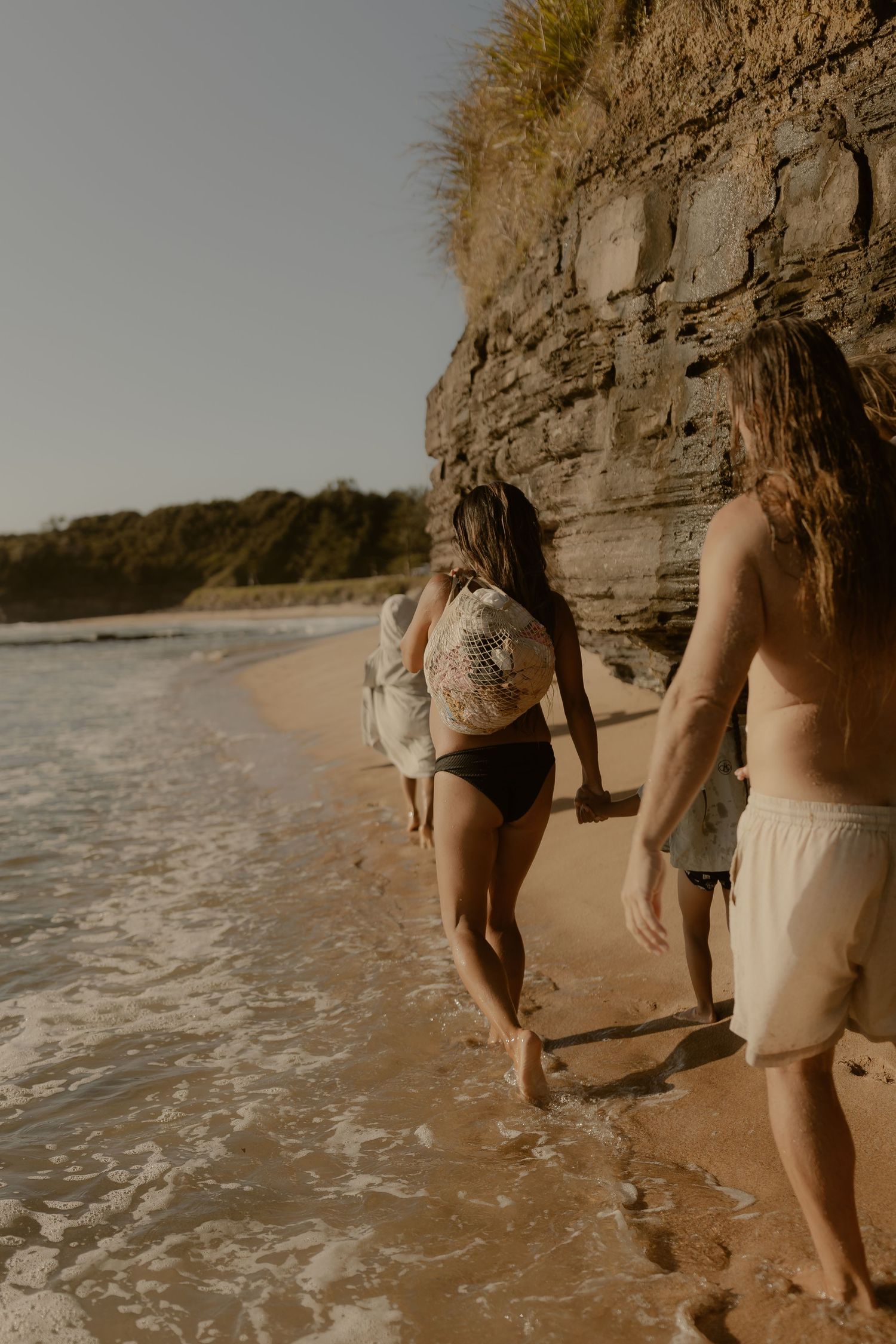 Group walking along a scenic beach shoreline with cliffs in the background during golden hour.