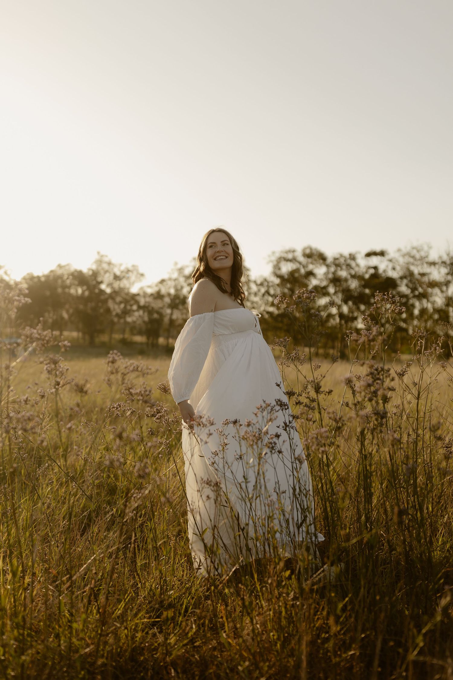 A dreamy sunset portrait in a wildflower field with a flowing white off-shoulder dress creating an ethereal atmosphere.