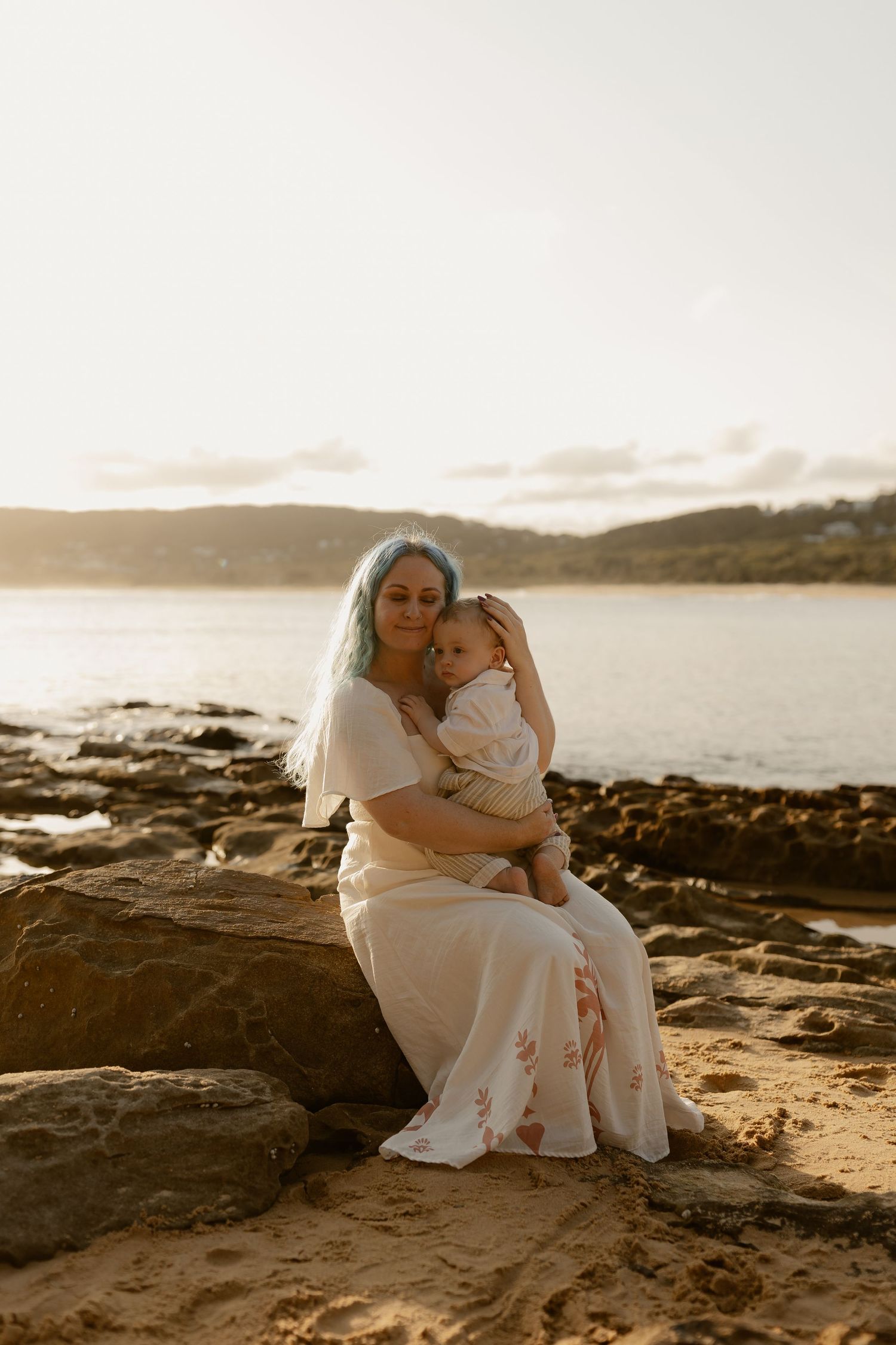 Tender sunset moment captured on rocky coastal beach with soft golden light illuminating the scene.