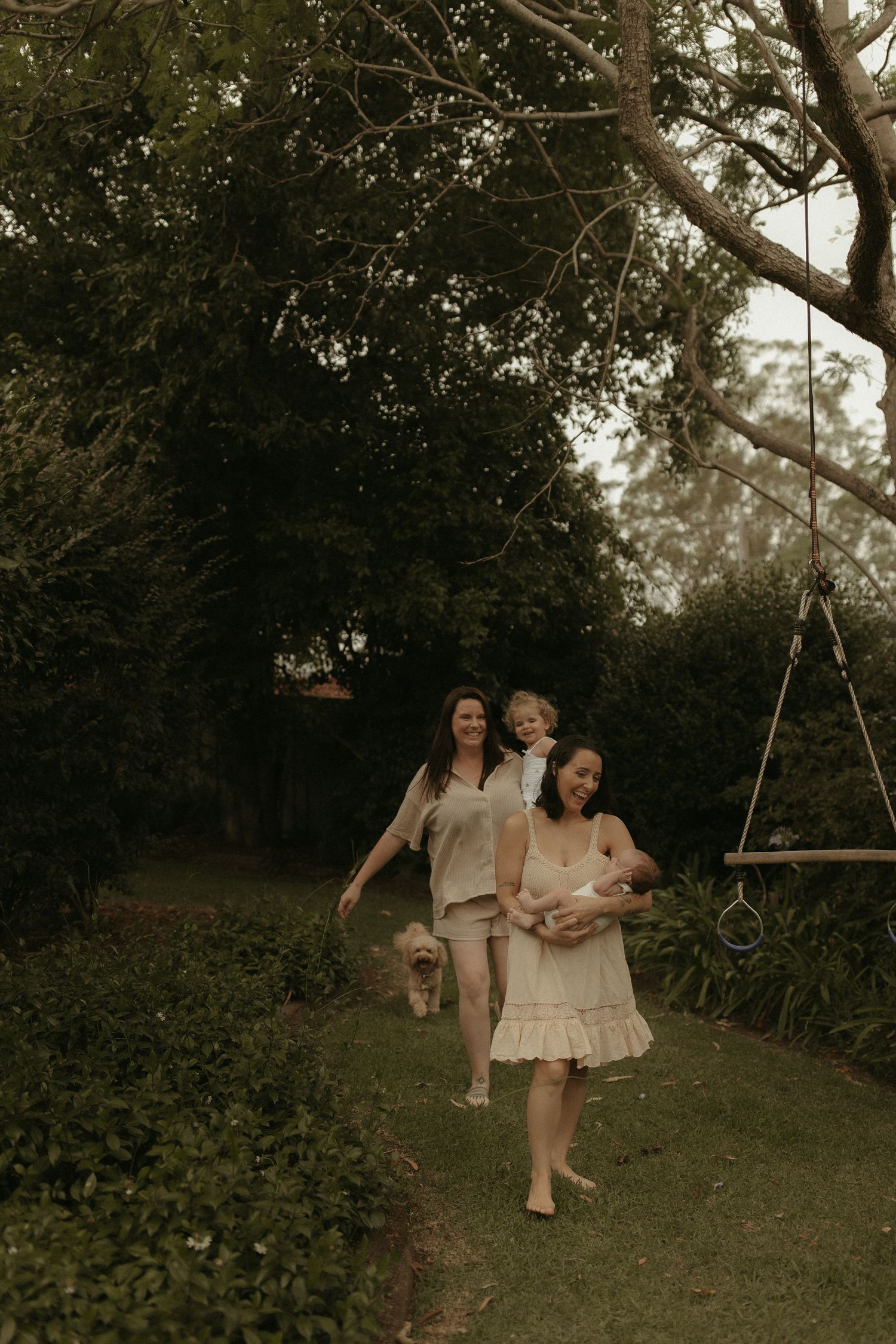 People enjoying a playful moment together on a tree swing in a lush garden setting at dusk.