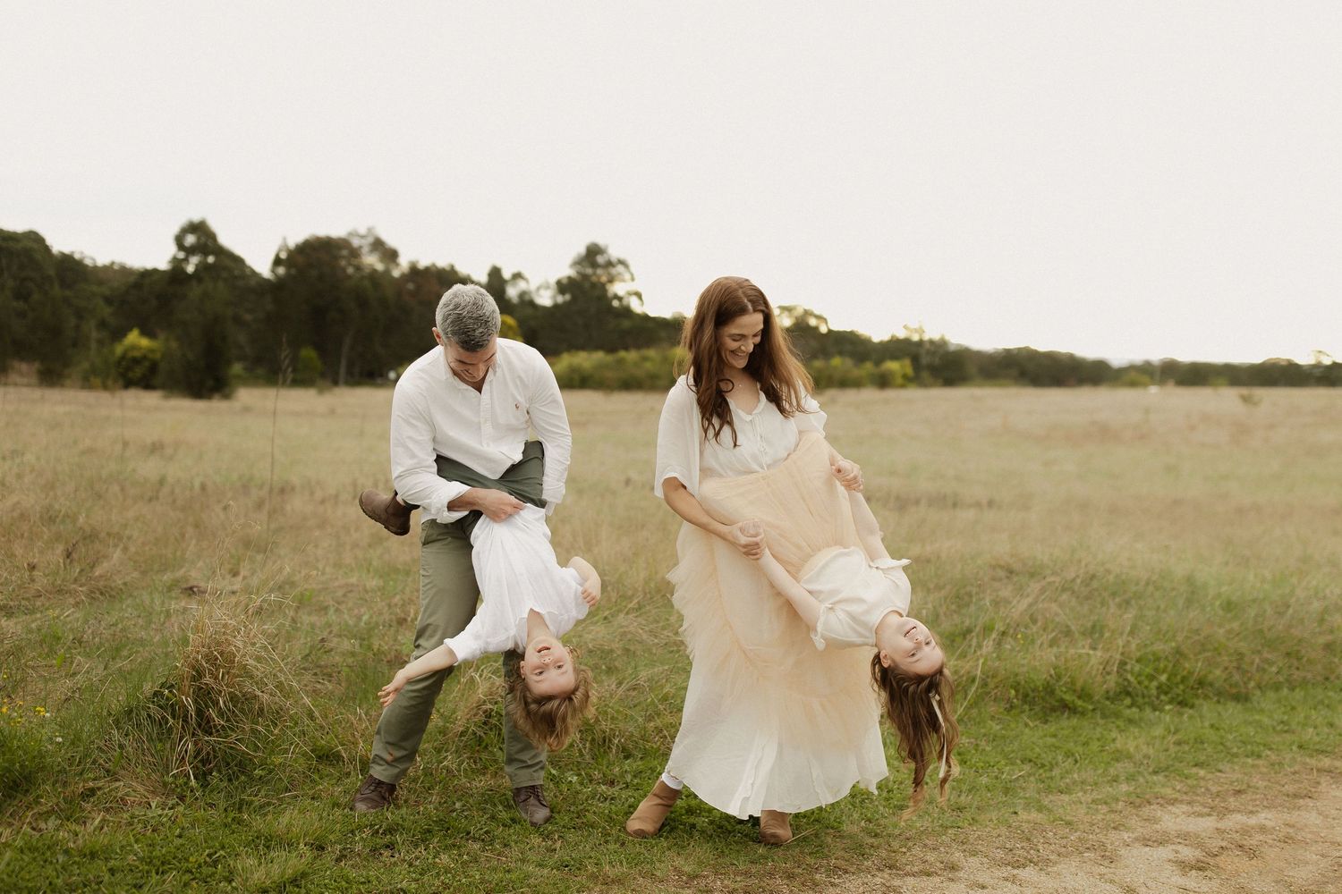 Friends dancing and playing together in white dresses on a scenic hilltop path during golden hour.