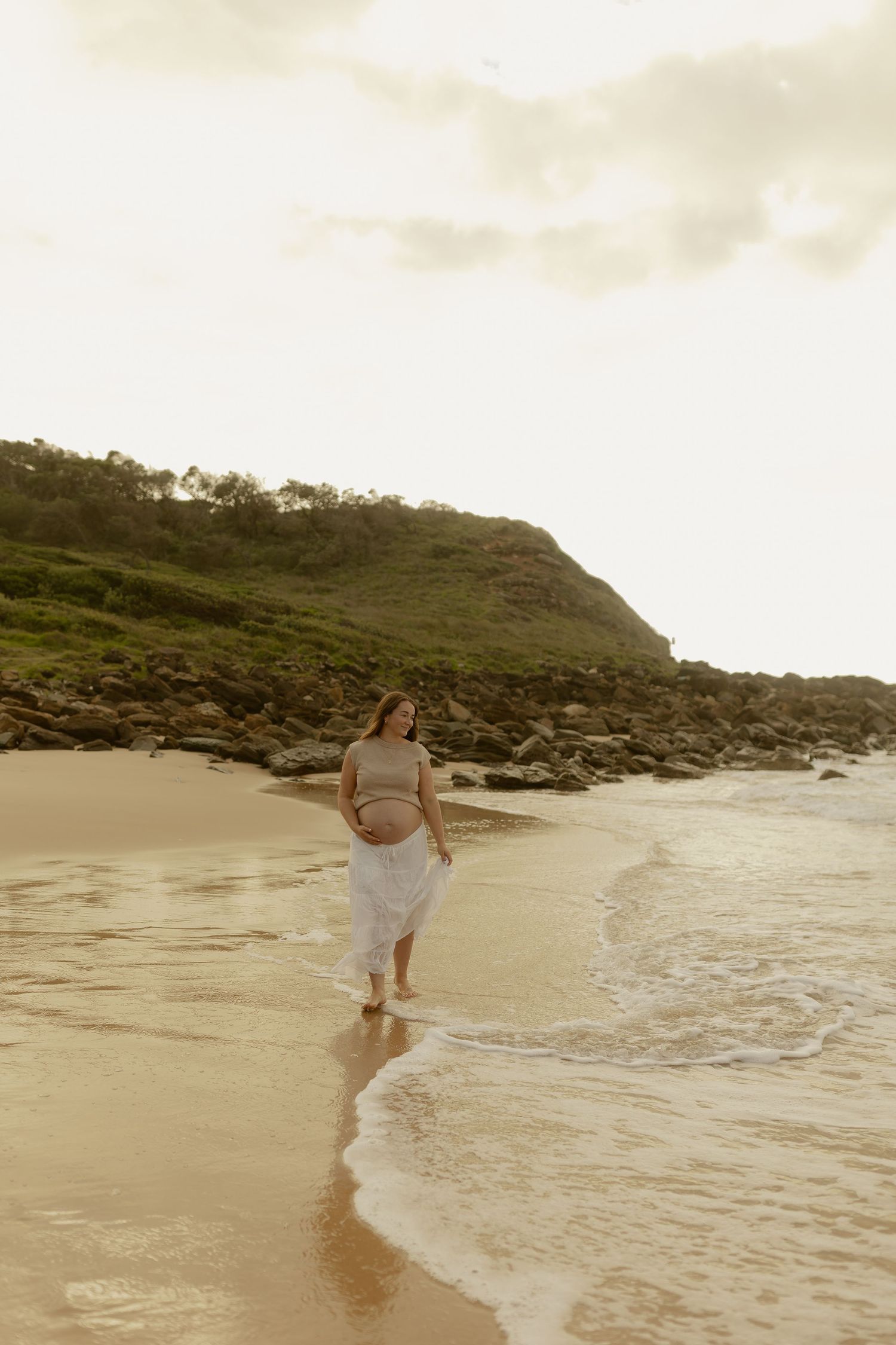 People playing and splashing in shallow ocean waves along scenic beach at sunset.