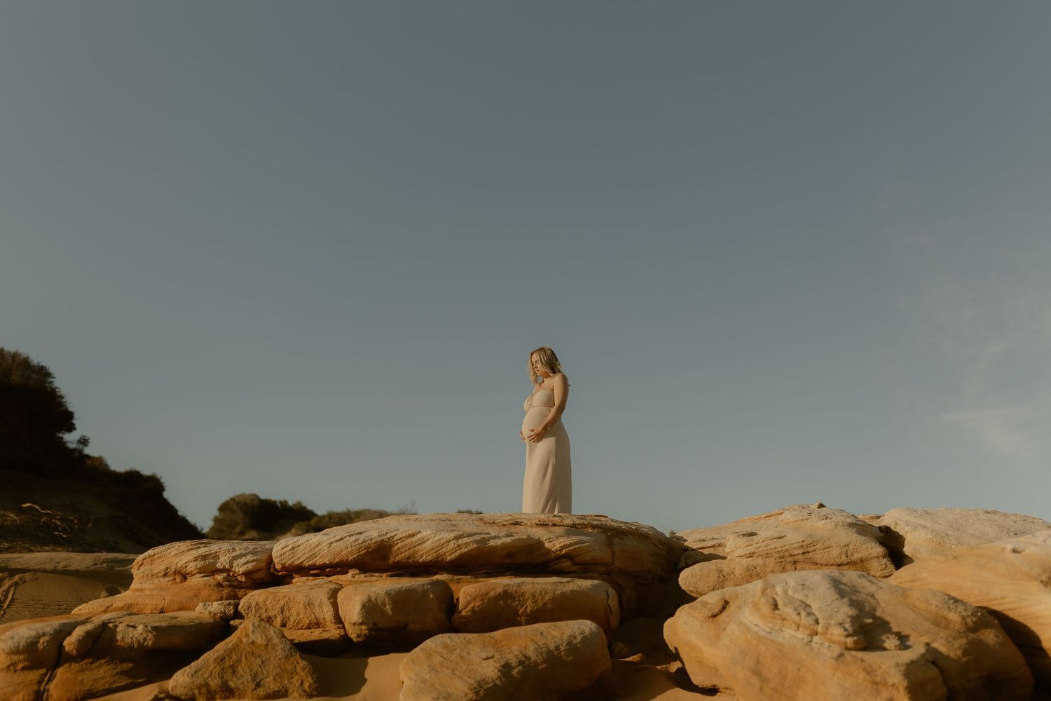 A figure stands atop rocky cliffs overlooking a scenic desert landscape at sunset.