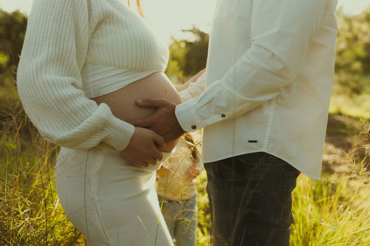 Two people in white sweaters standing close together in a warm golden field.