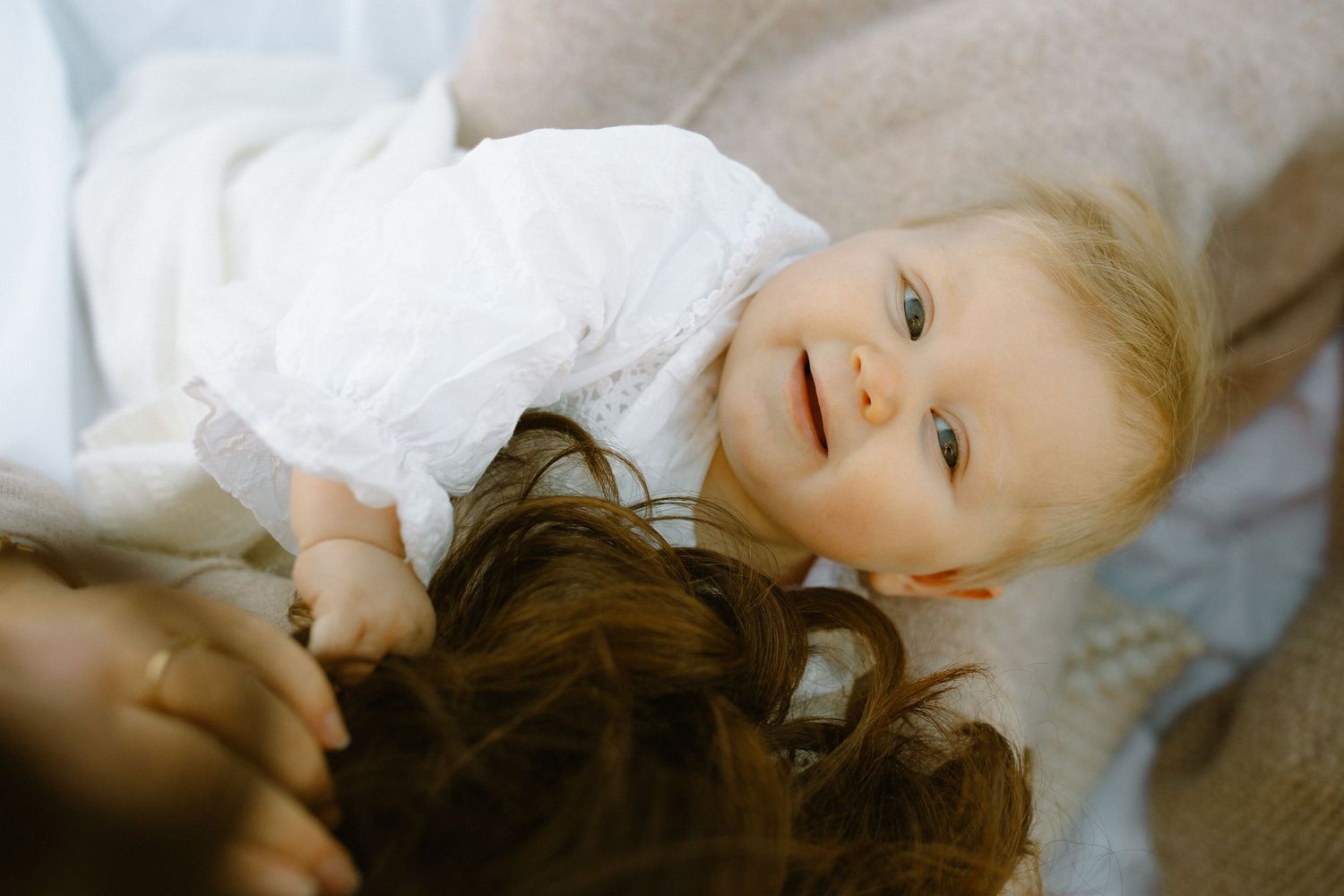 Baby wearing white outfit lies on soft bedding during intimate lifestyle photography session.