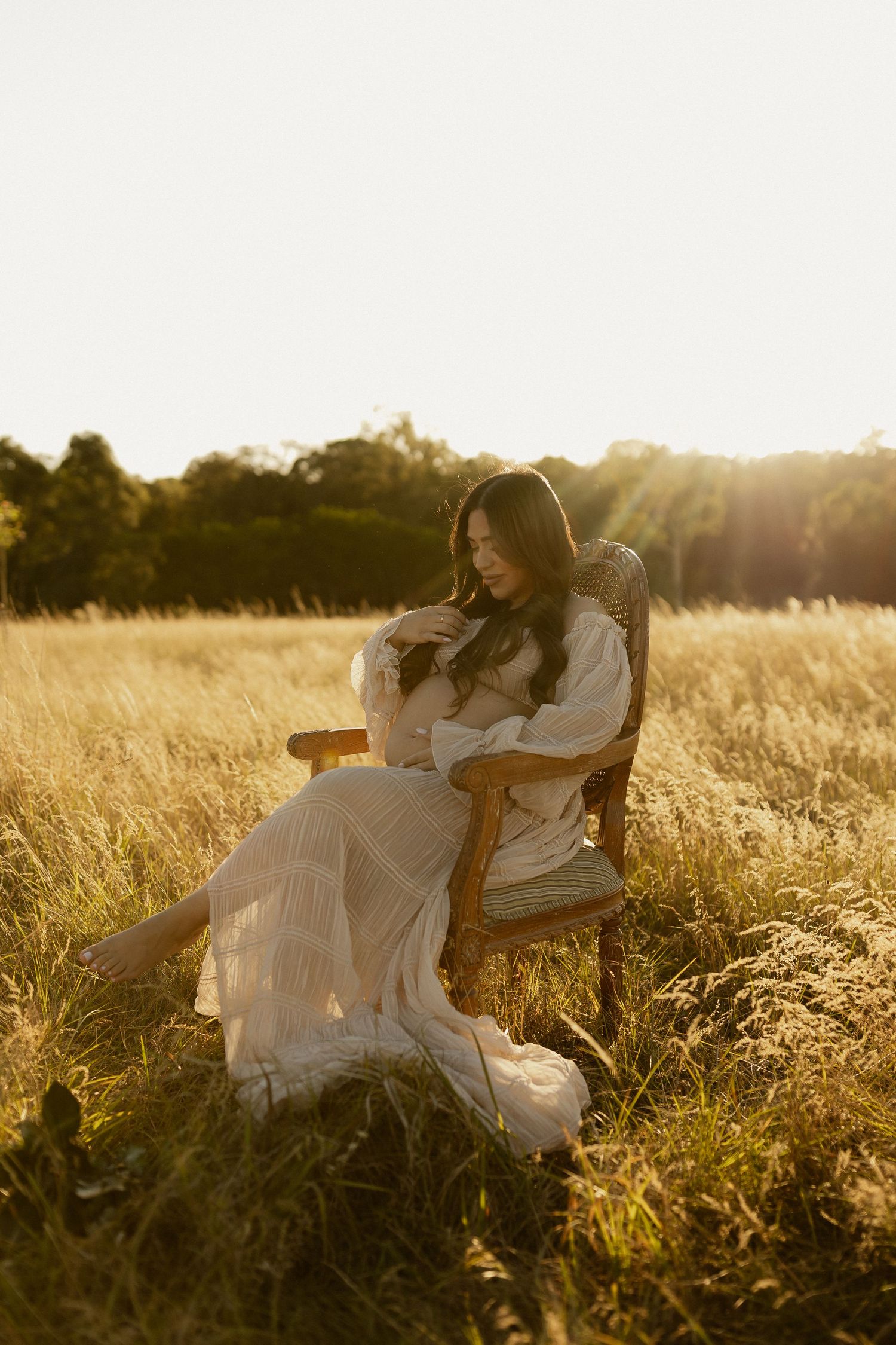 Two people in white dresses relax on a wooden bench in a sunlit meadow during golden hour.