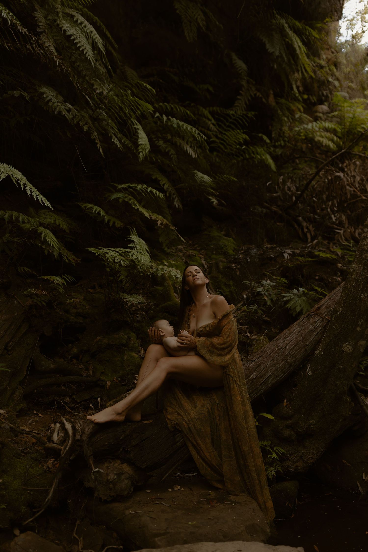 Artistic portrait in moody forest setting with ferns and fallen logs creating ethereal woodland atmosphere.