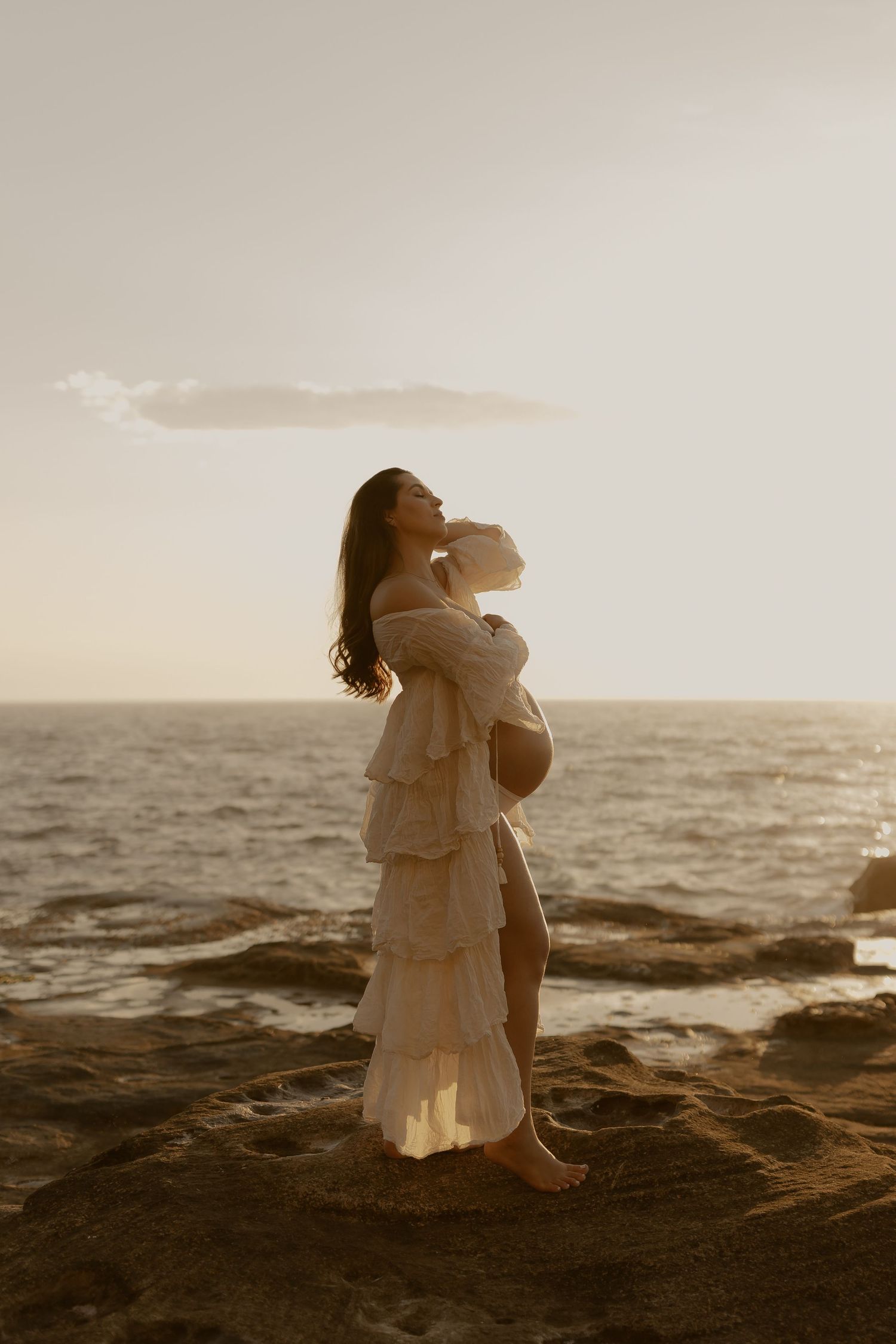 A sepia-toned sequence shows a figure in a flowing white dress dancing on rocky coastal cliffs at sunset.
