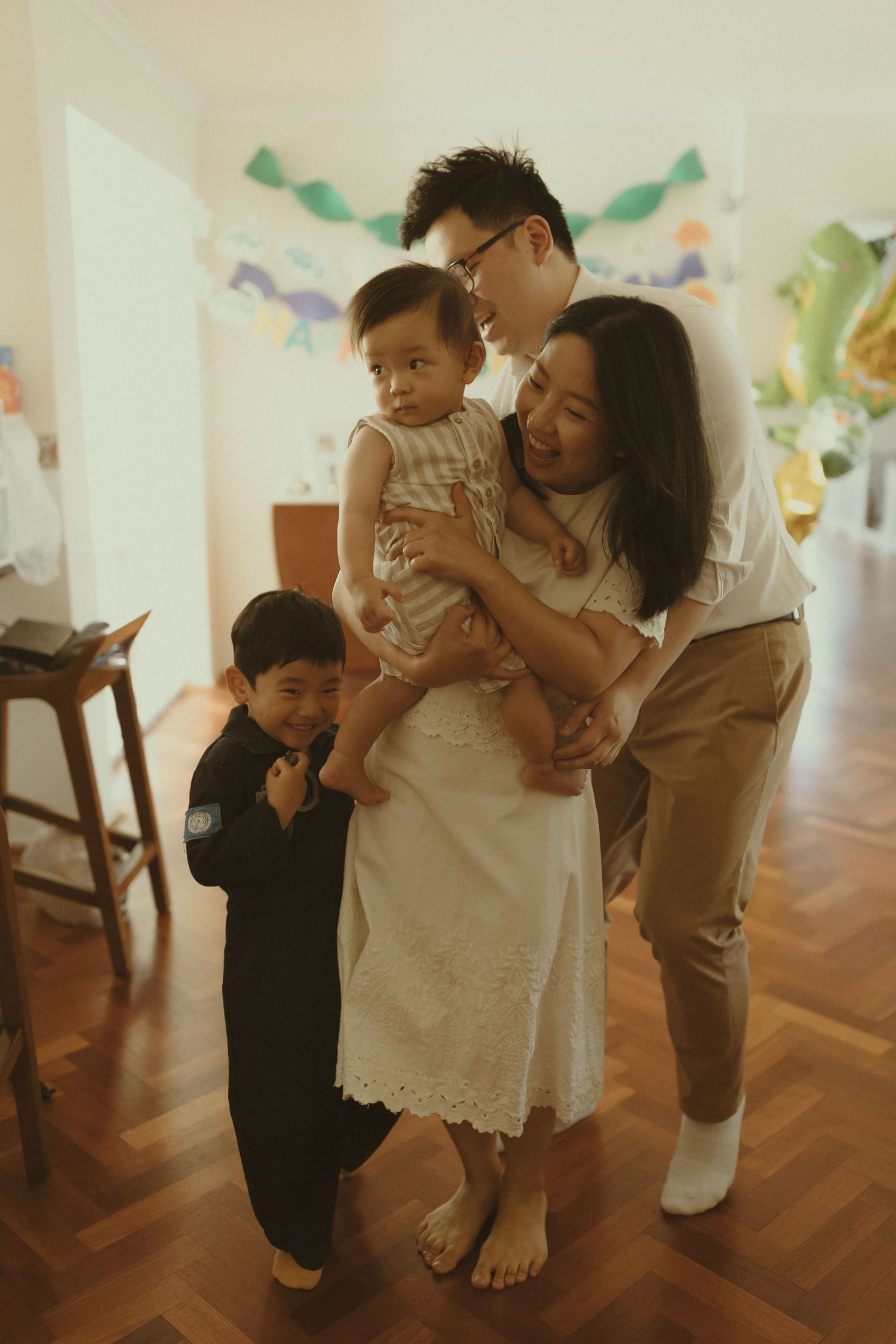 Family playing and bonding together on hardwood floors with festive decorations visible in the background.